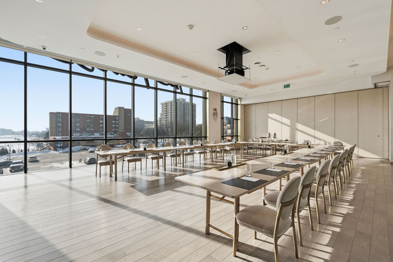 Modern cafeteria interior with rows of white tables and chairs next to floor-to-ceiling windows offering natural light.
