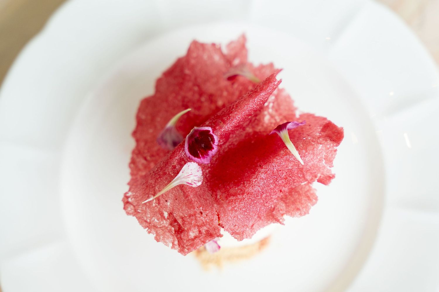 Pink cotton candy or spun sugar dessert presented on a white plate.