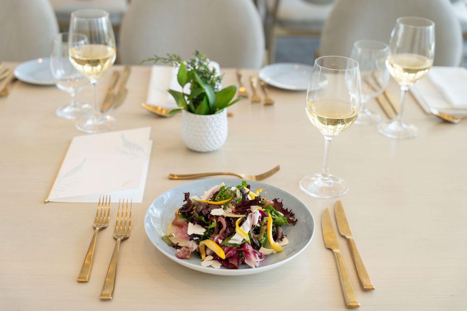 Elegant plated meals served on white dishes at an upscale restaurant with wine glasses and gold cutlery.