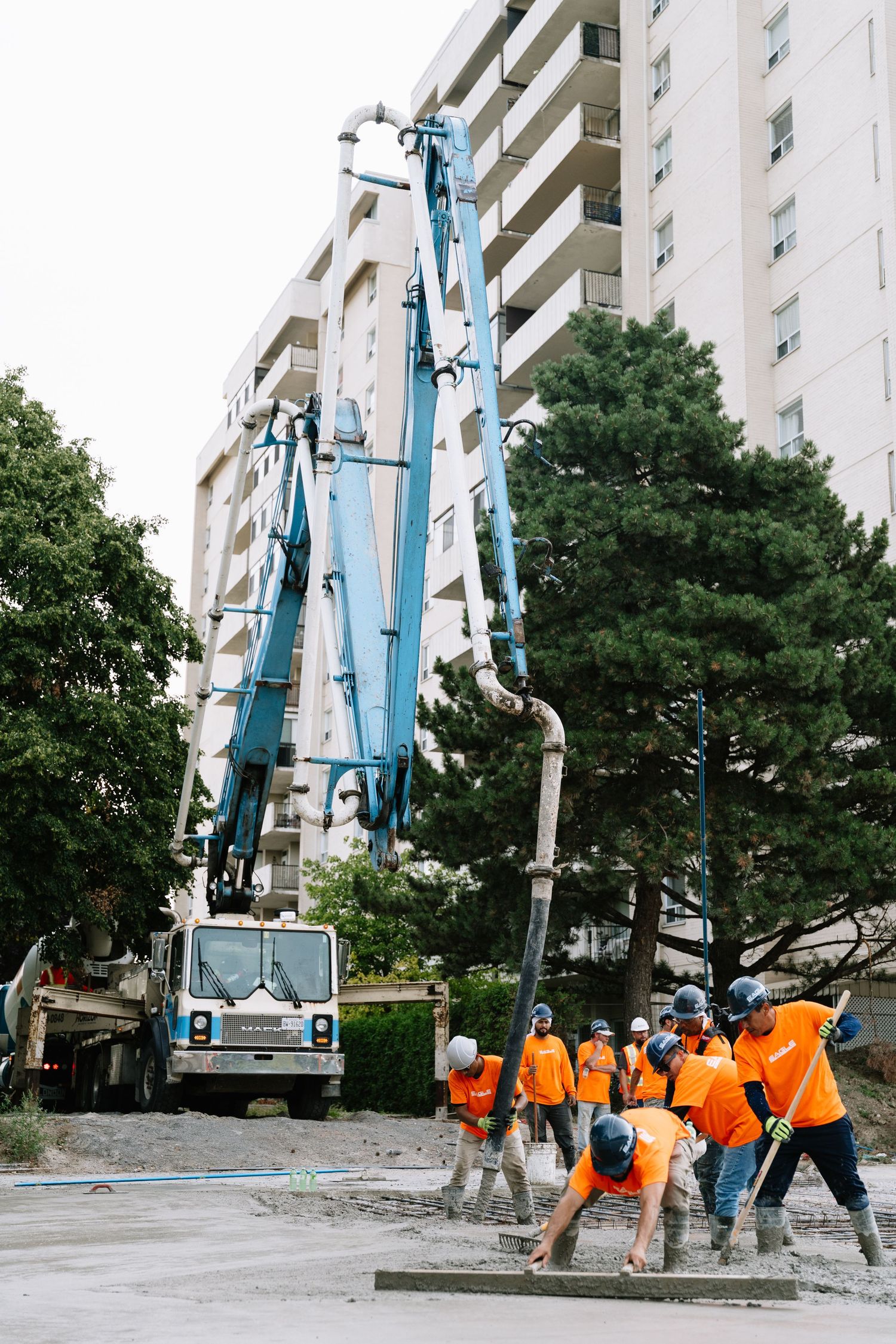 Workers in orange vests gather near a tall apartment building with a large crane visible against the blue sky.