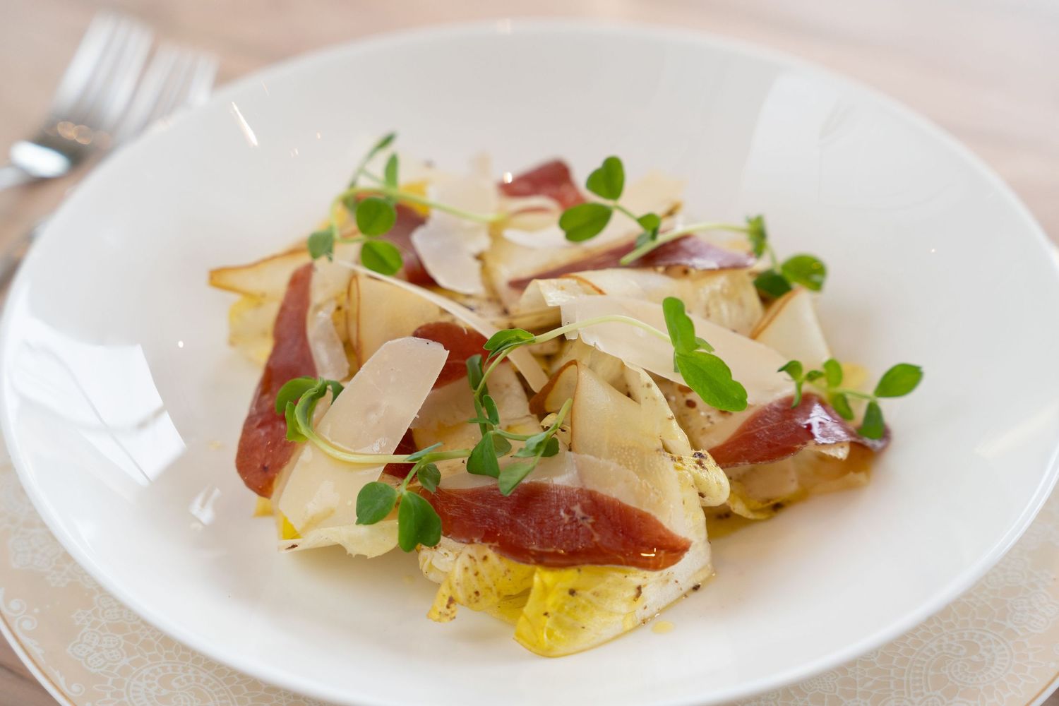 Elegant plated appetizer with thin sliced meat, microgreens and shaved cheese.