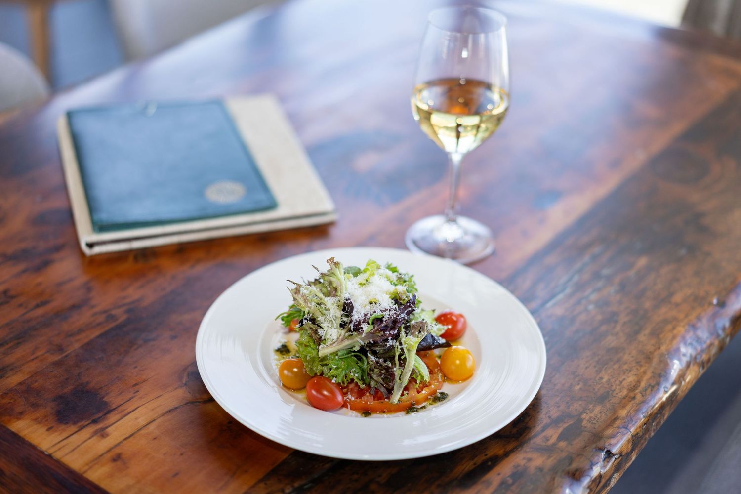 Fine dining dishes arranged on a rustic wooden table with wine glasses and decorative elements.
