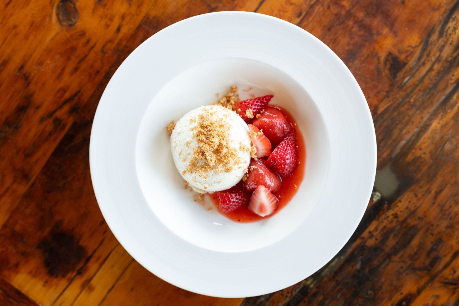 Fresh strawberries and whipped cream dessert served on white plates against a rustic wooden table surface.