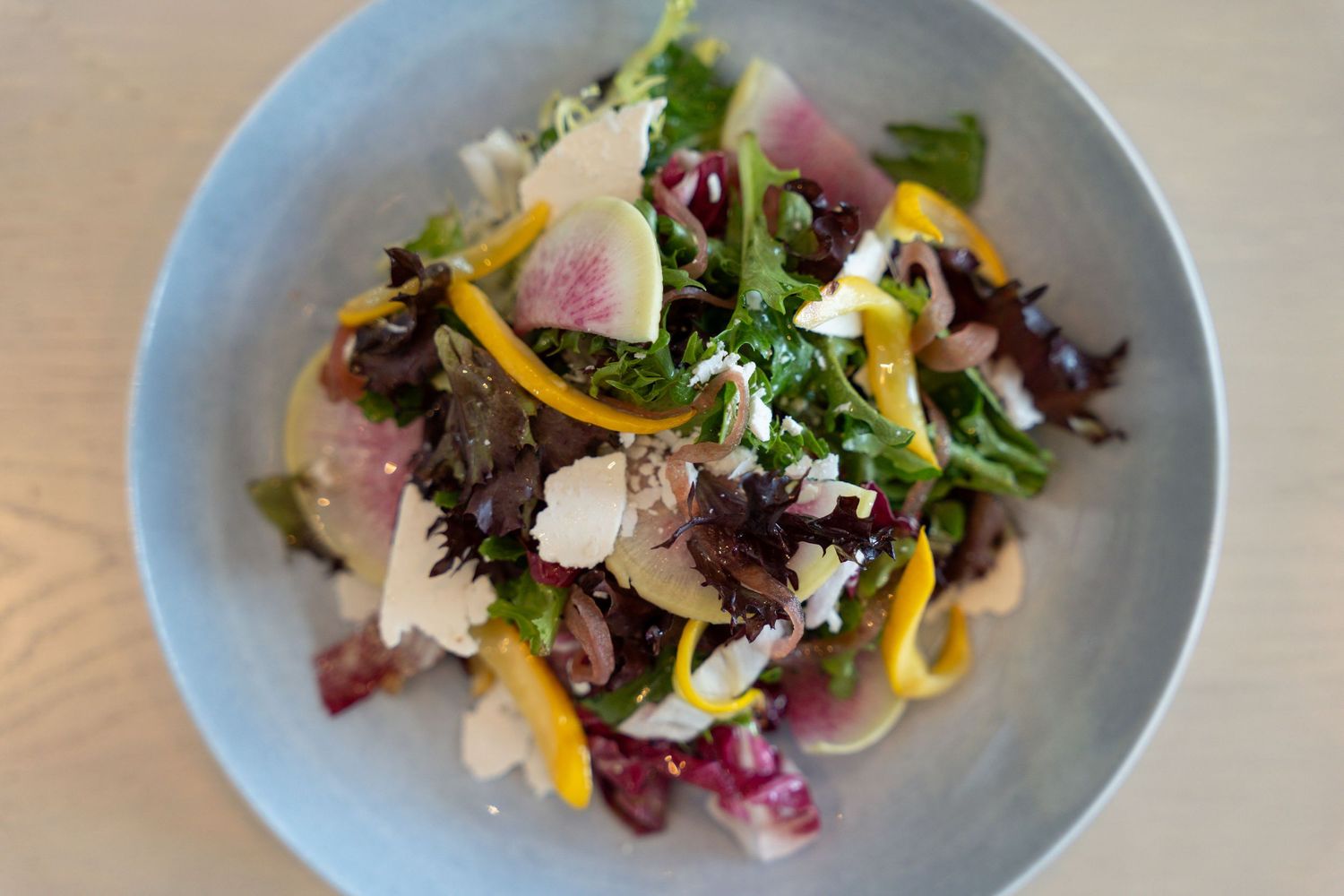 Four identical plates of artfully plated salads with colorful greens, edible flowers, and garnishes arranged in a row.