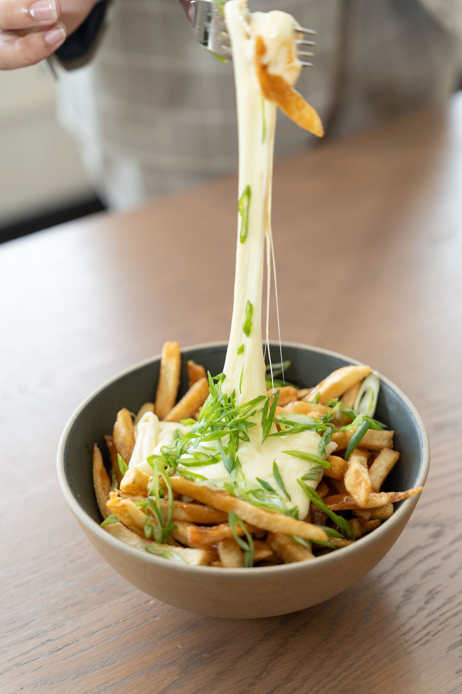 Stretchy melted cheese pulls away from a bowl of french fries garnished with fresh herbs.