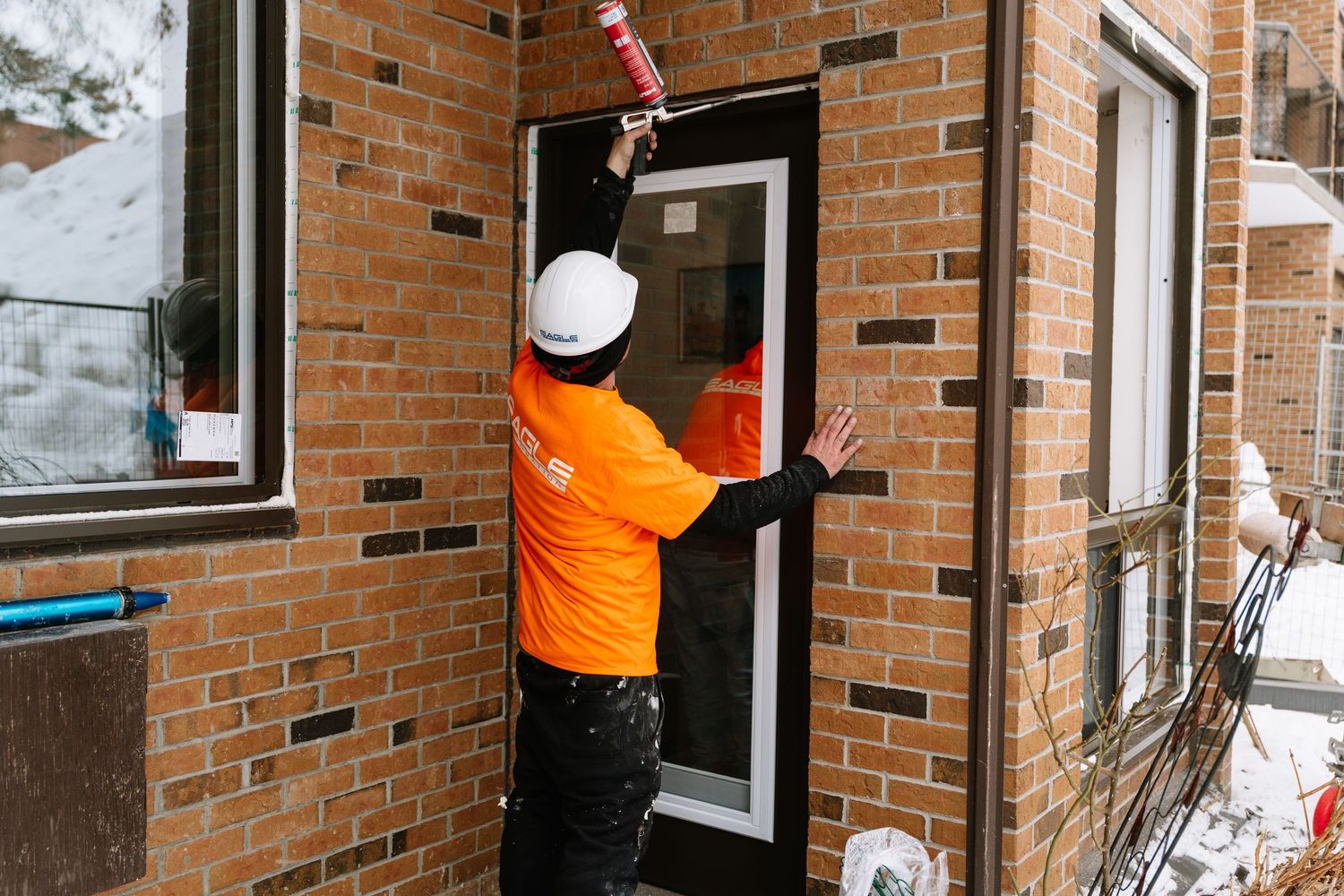 Window cleaning crew in orange uniforms service multiple windows on a residential building.