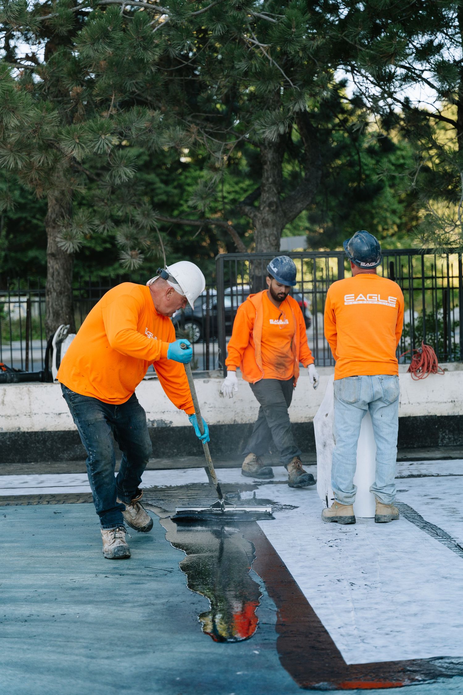 Construction workers in orange safety shirts install roofing material on a flat surface during a commercial project.