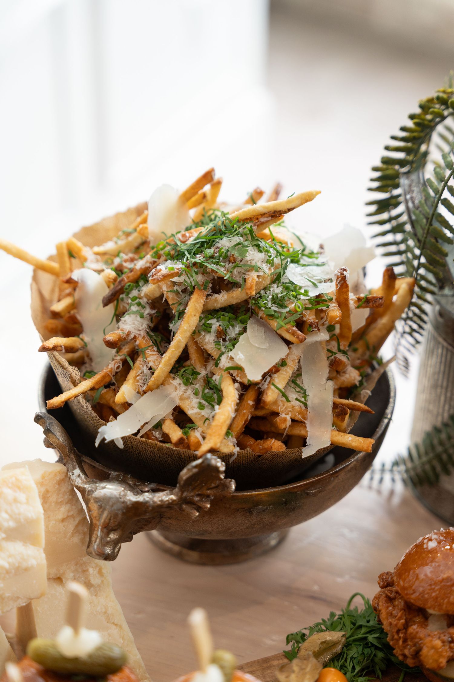 Crispy shoestring potatoes topped with fresh herbs and shaved cheese served in a dark bowl.