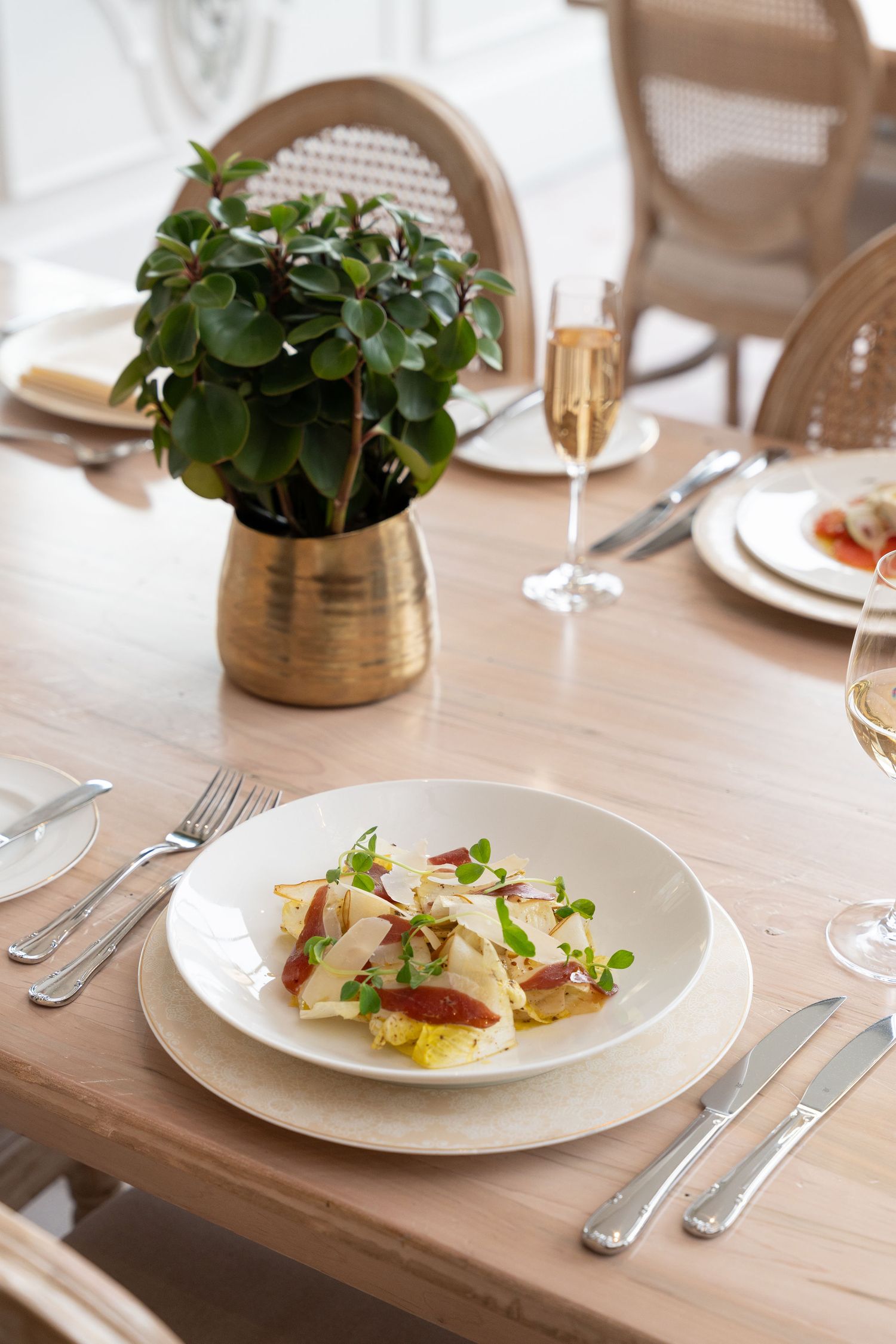 Elegant table setting with a plated dish, golden vase with green plant, and champagne glass on wooden table.
