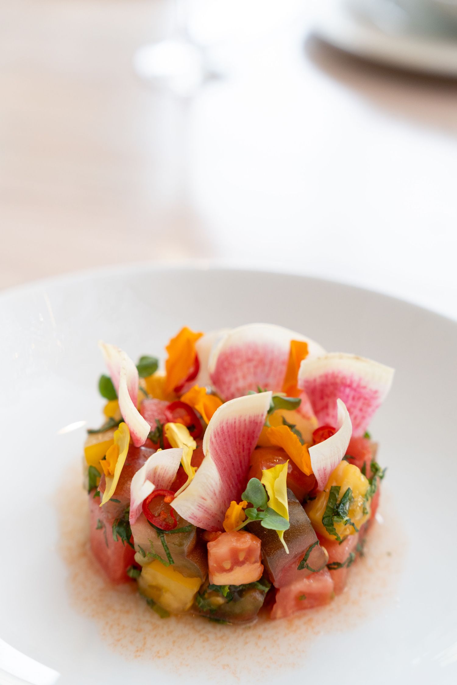 Artfully plated sashimi with colorful garnishes arranged in a modern style on a white plate.