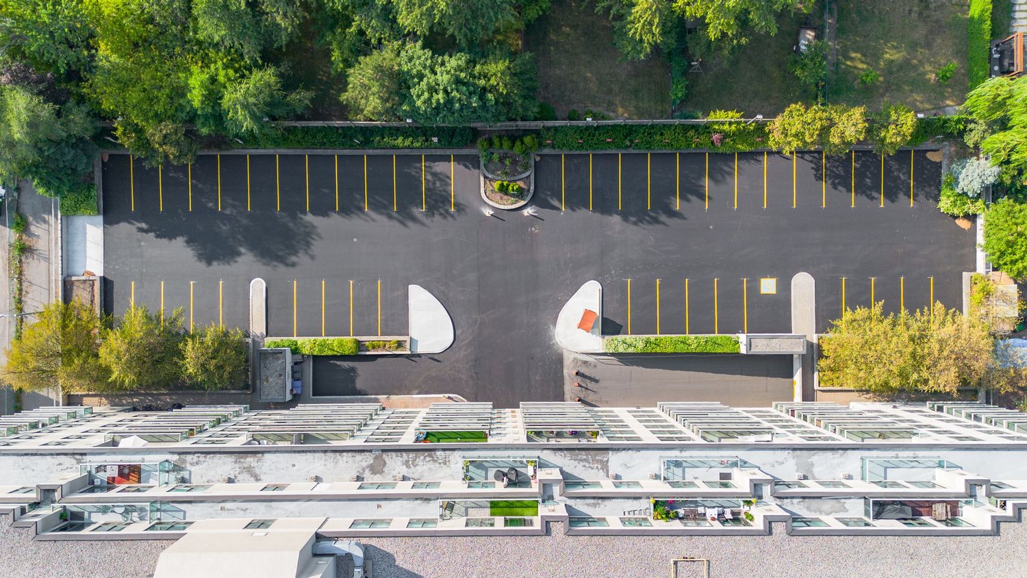 Aerial panoramic view of a large parking lot with cars surrounded by green trees and buildings.