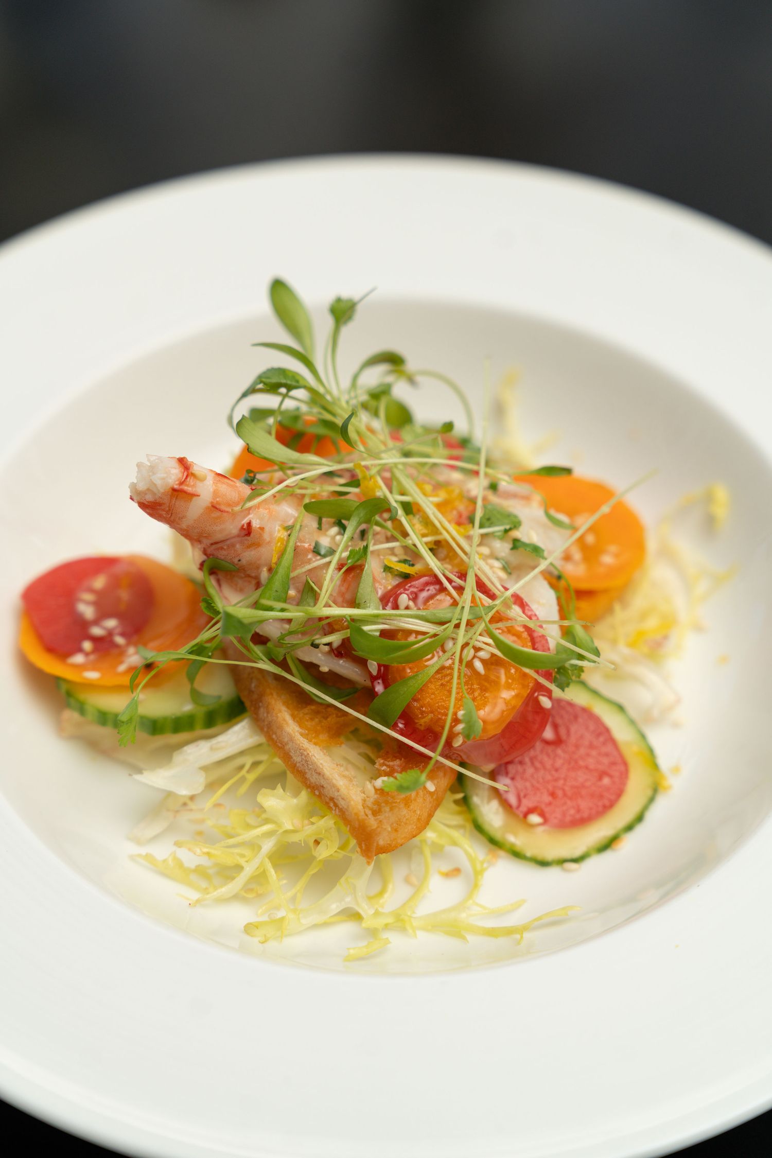 Elegant plated appetizer with thinly sliced fish, citrus, and microgreens arranged on white dishes.