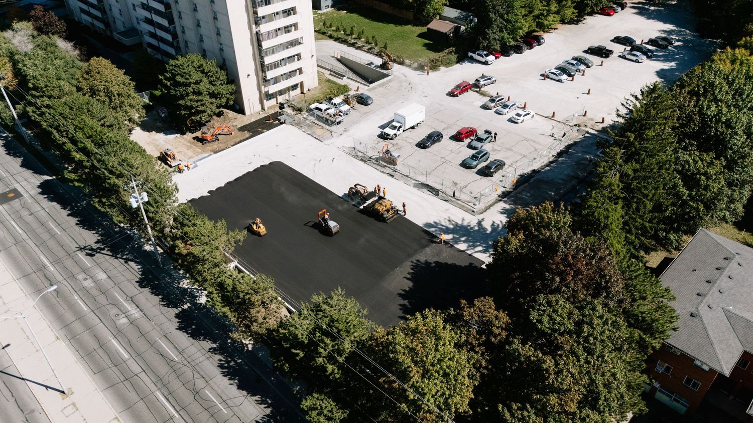 Aerial view of urban buildings, parking lots, and tree-lined streets on a sunny day.