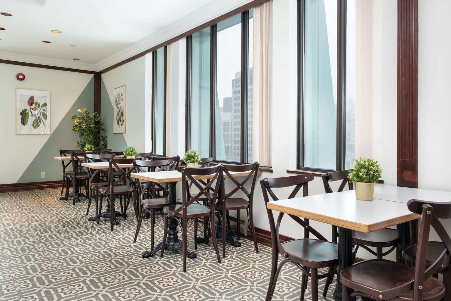 Modern cafe interior with dark wooden tables and chairs arranged in a bright space with large windows and geometric flooring.