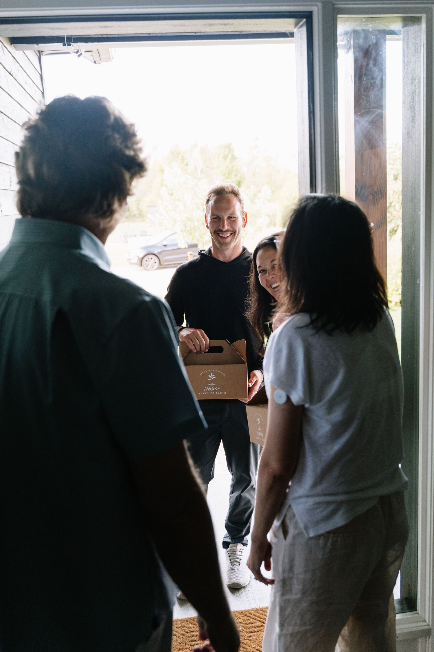 Delivery person standing at doorway with package while residents greet them at home entrance.