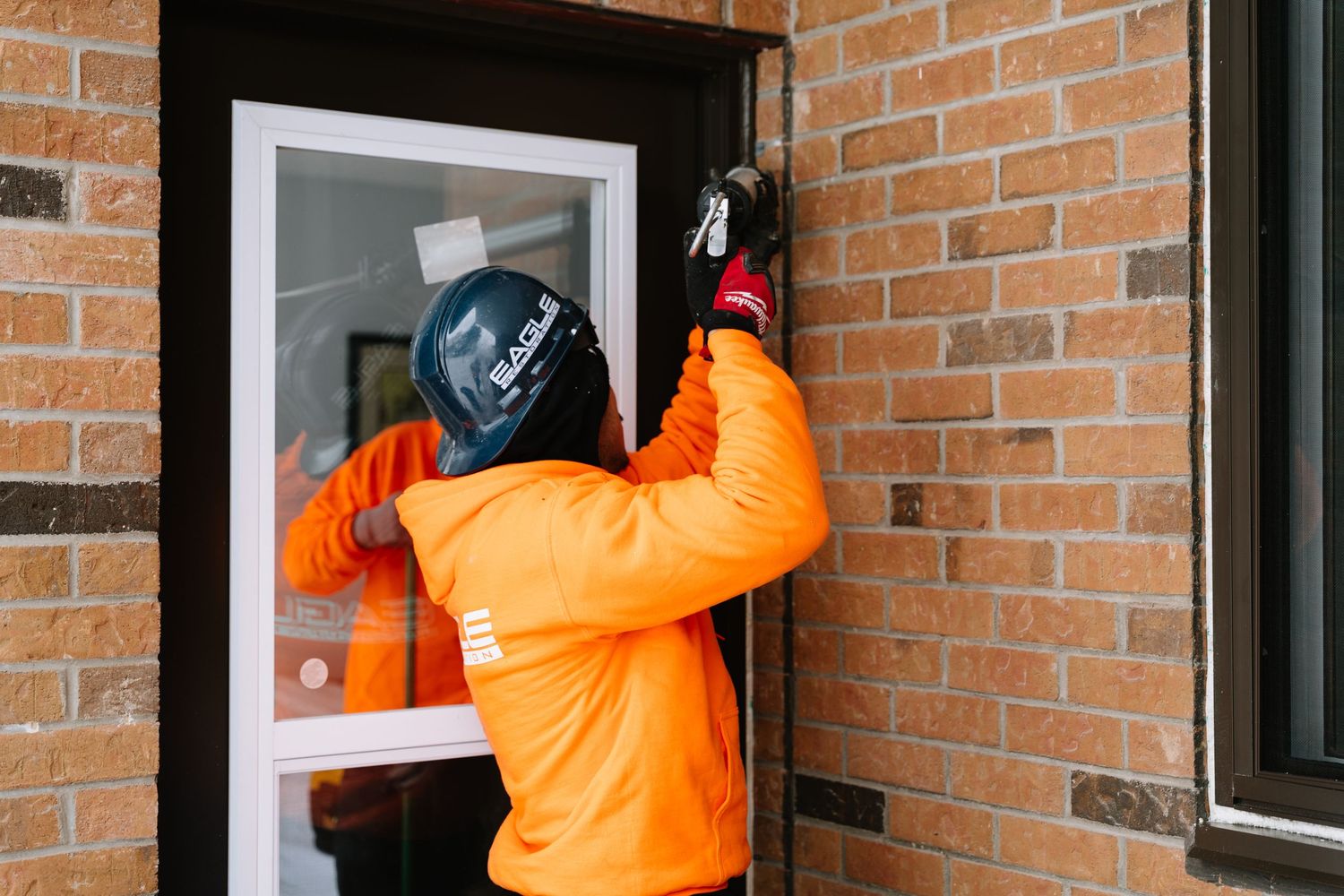Maintenance crew member in orange safety gear works on exterior window frames.