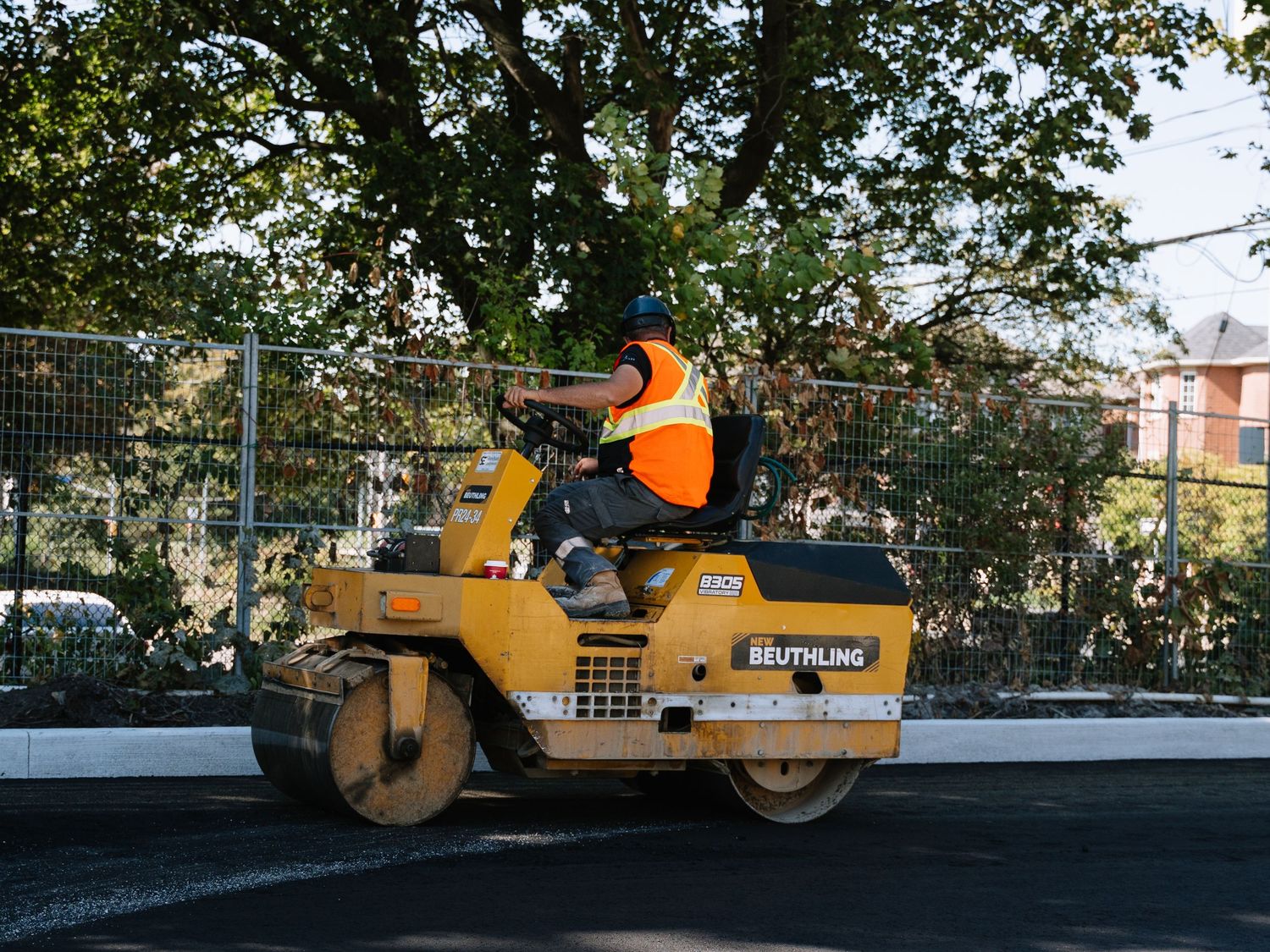 Heavy construction equipment including rollers and compactors parked on fresh asphalt at a paving site.