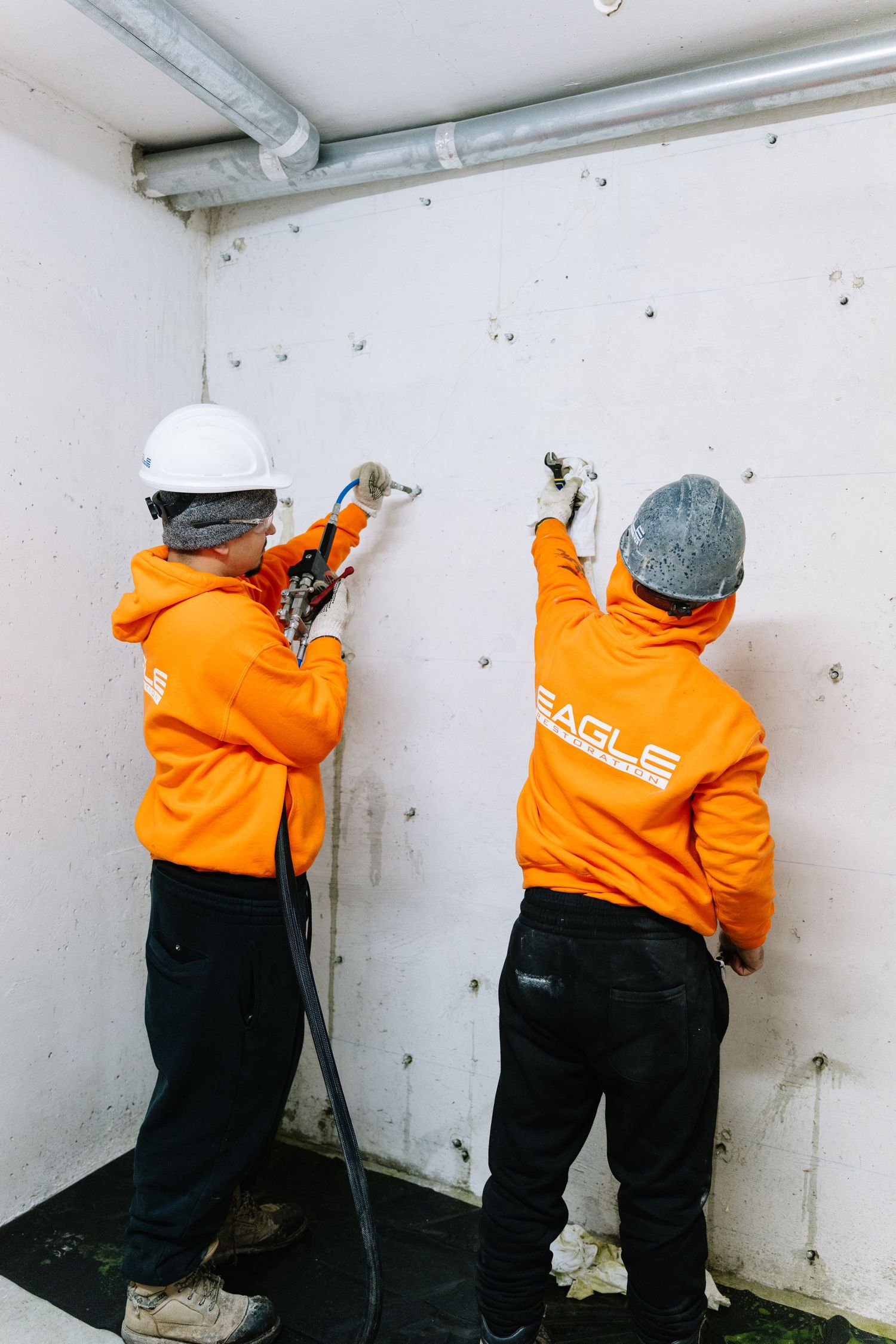 Worker in orange safety vest and hard hat drilling into white wall during construction or renovation project.