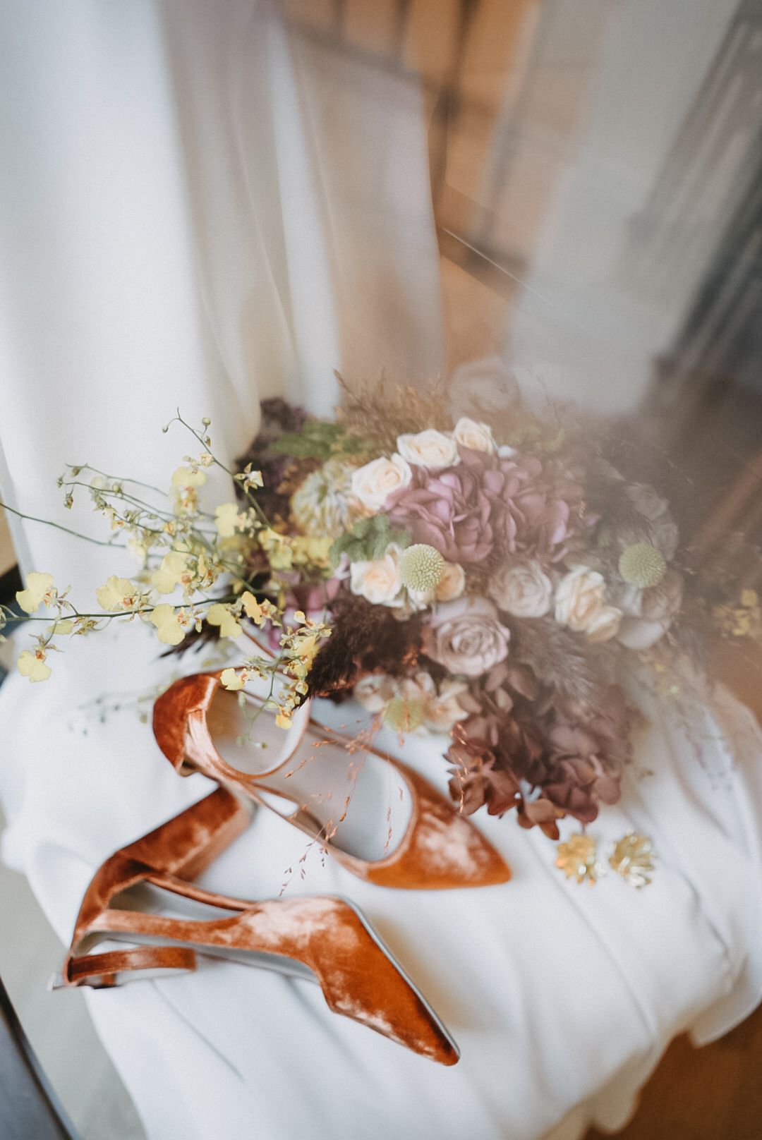 Delicate floral arrangements with roses and orchids displayed on white fabric with copper-colored accents.