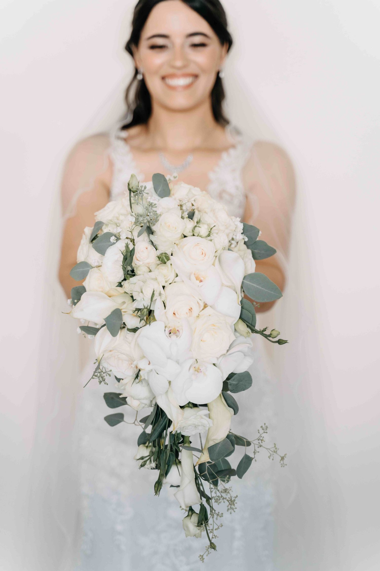 Beautiful cascading white bridal bouquet with roses, white orchids and eucalyptus against a light background.