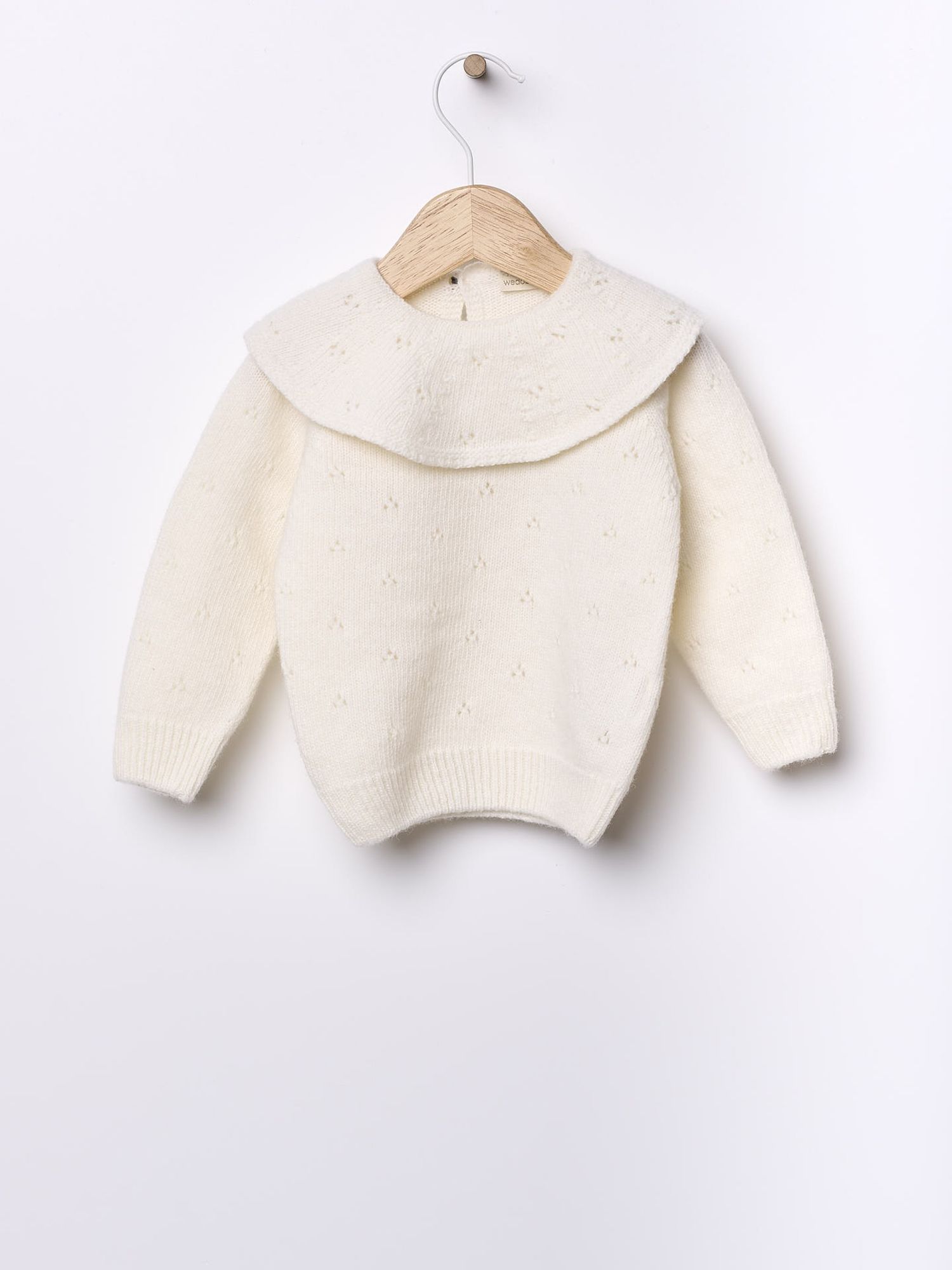 Cream-colored knit sweater with peter pan collar on wooden hanger against white background.