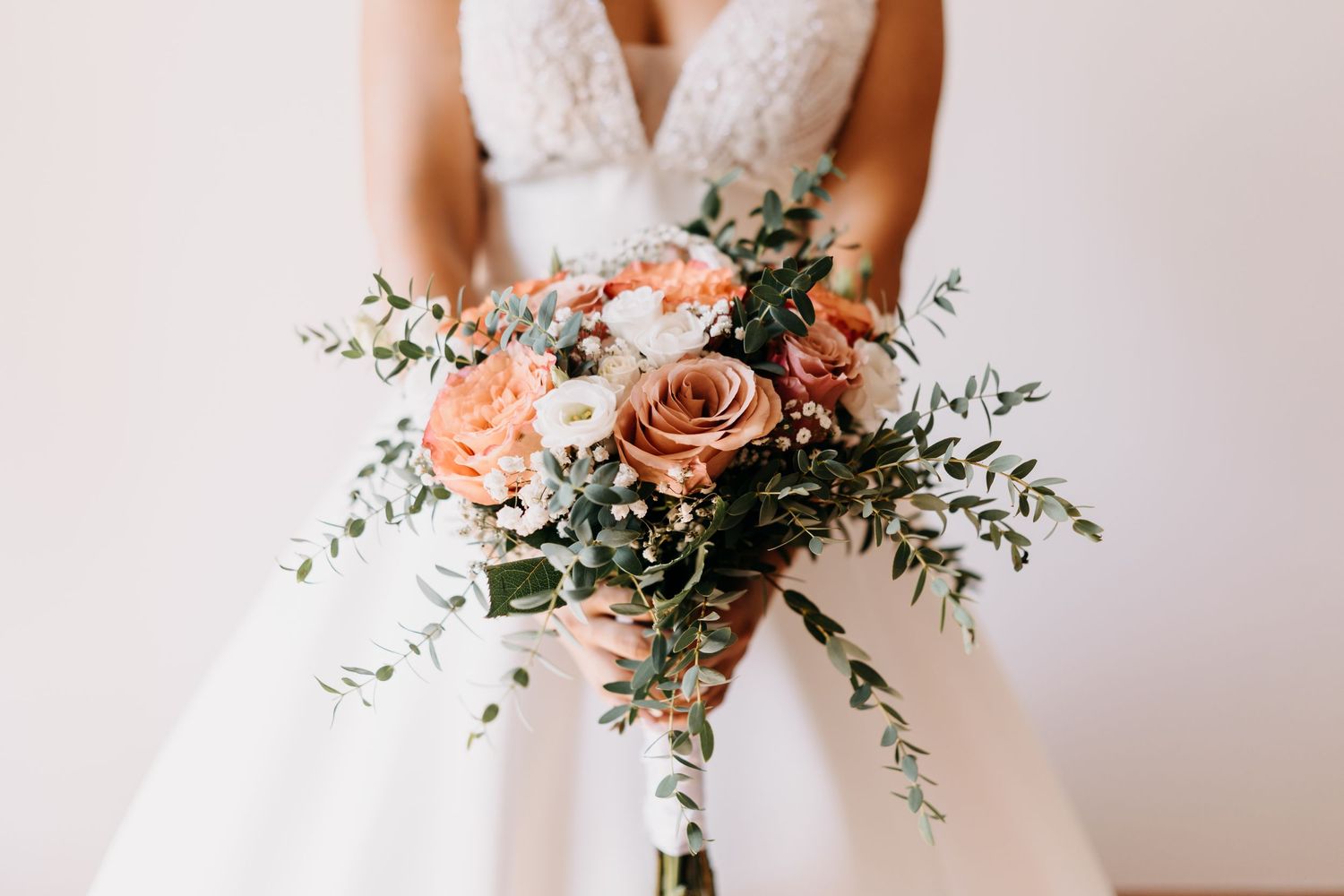 A delicate bridal bouquet featuring peach and blush roses with flowing eucalyptus greenery against a white backdrop.