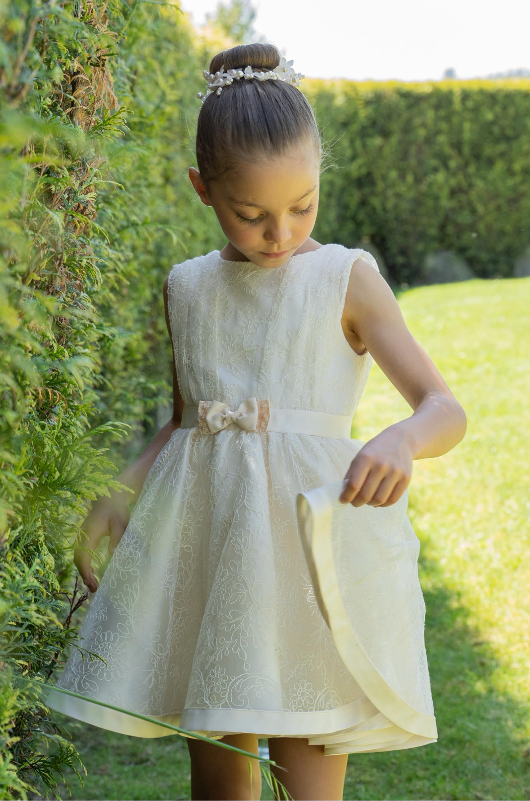 A sleeveless ivory dress with floral embellishments and a gathered waist stands out against a lush garden backdrop.
