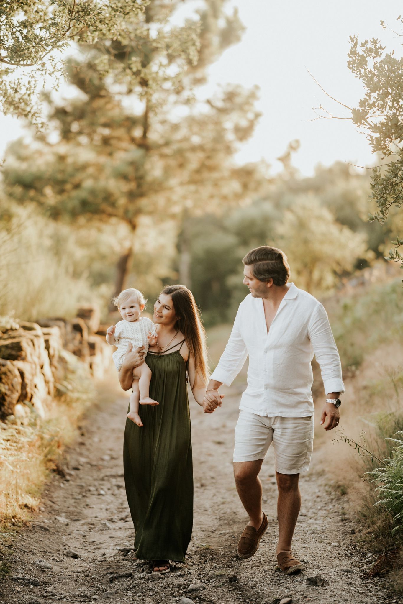 Family walking together on a sunlit forest path during golden hour in coordinated white and black outfits.