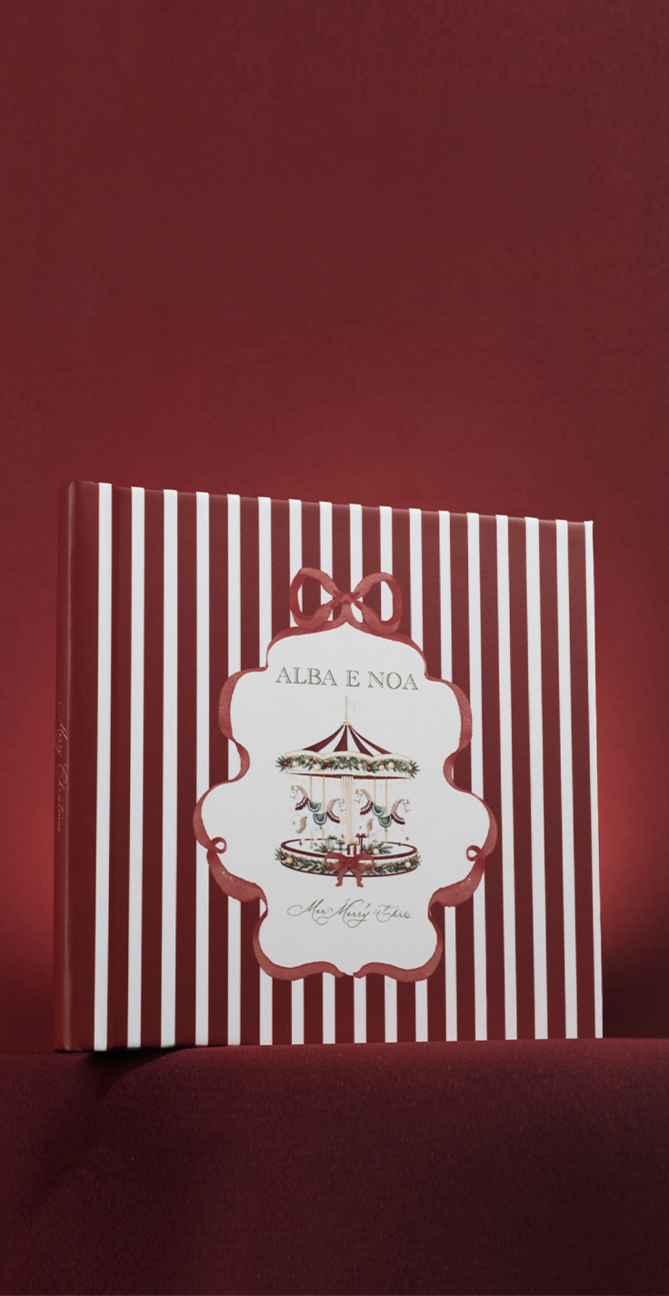 Red and white striped square book titled Alba E Noa featuring a carousel illustration and decorative bow on a dark red background.