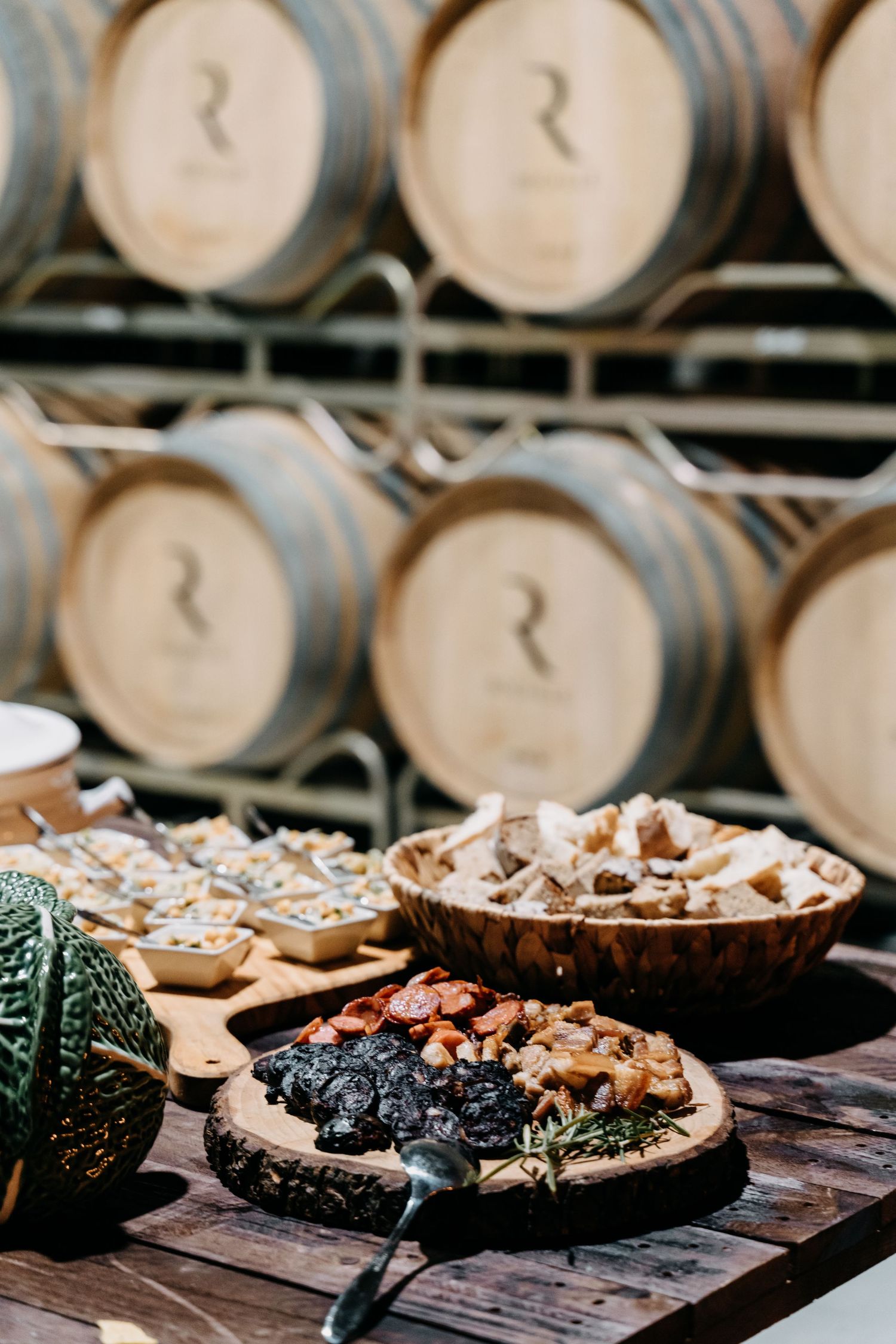 Wine barrels serve as backdrop to chocolate cakes displayed on wooden boards in rustic winery setting.
