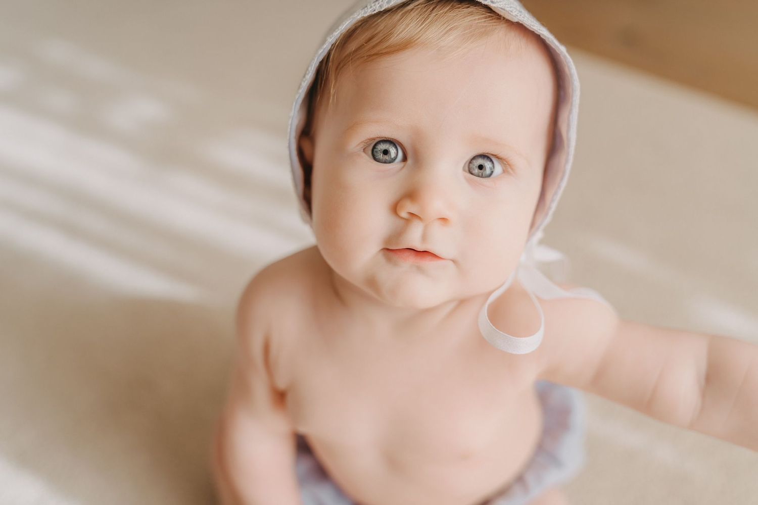 Baby wearing soft pink bonnet looking up with bright wide eyes.