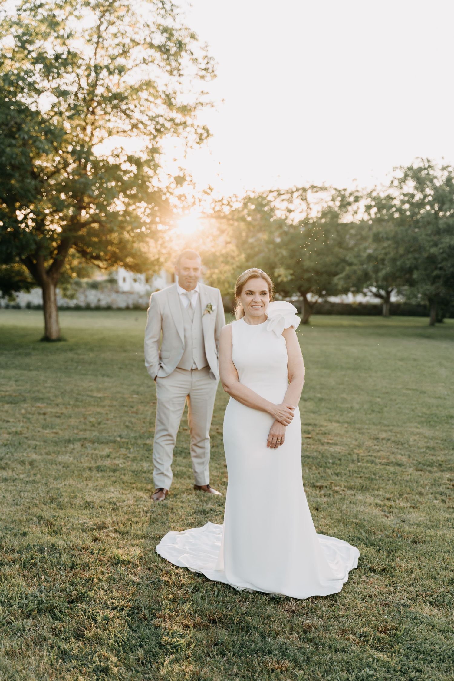 A romantic sunset wedding photo session in a grassy field with soft natural lighting and trees in the background.