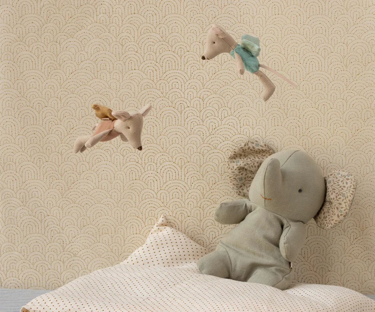 A soft plush elephant toy with angel wings rests on a bed while two small stuffed animals float above.