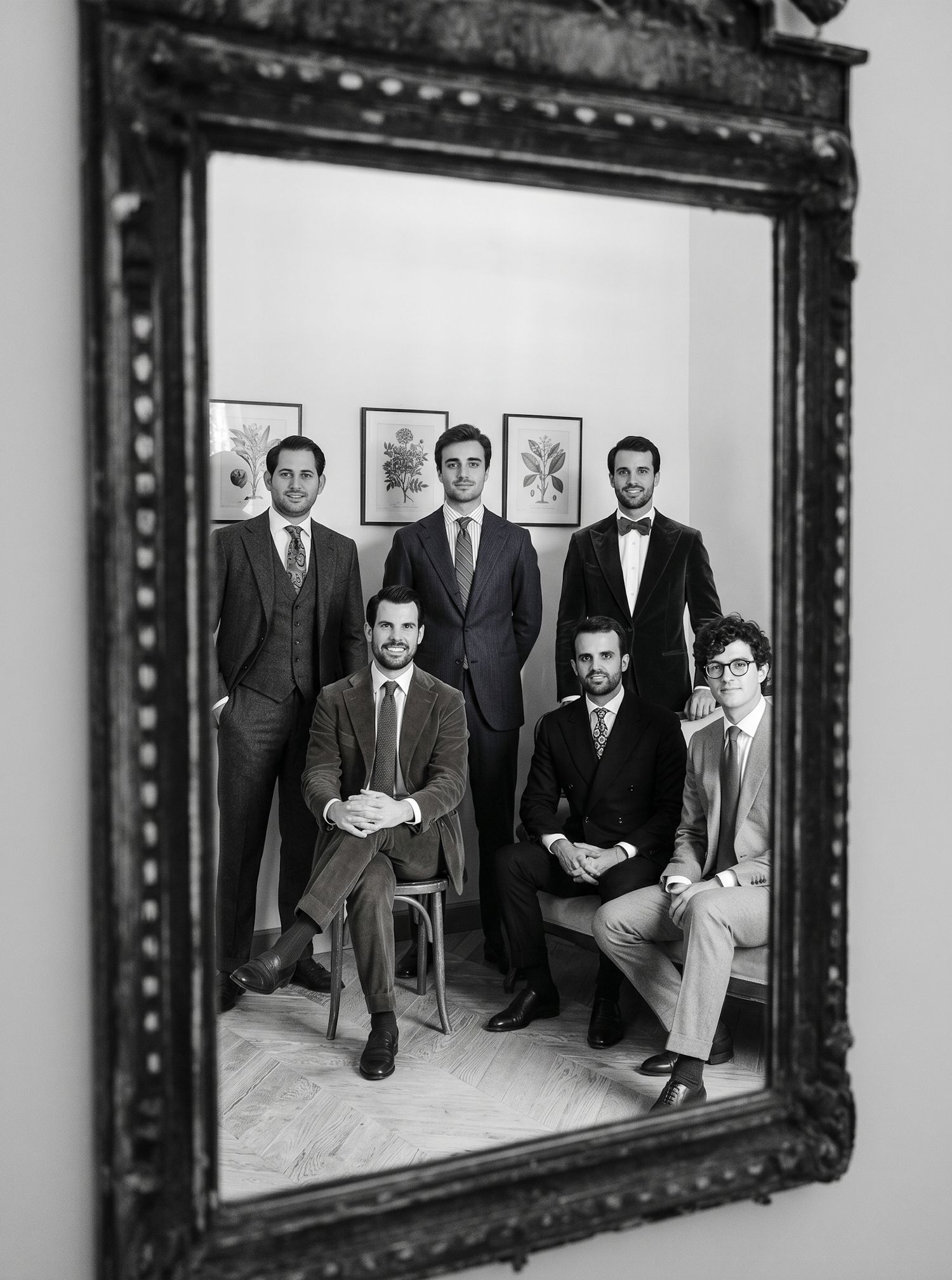 Black and white photo of six well-dressed men in suits posing formally in a mirror reflection.