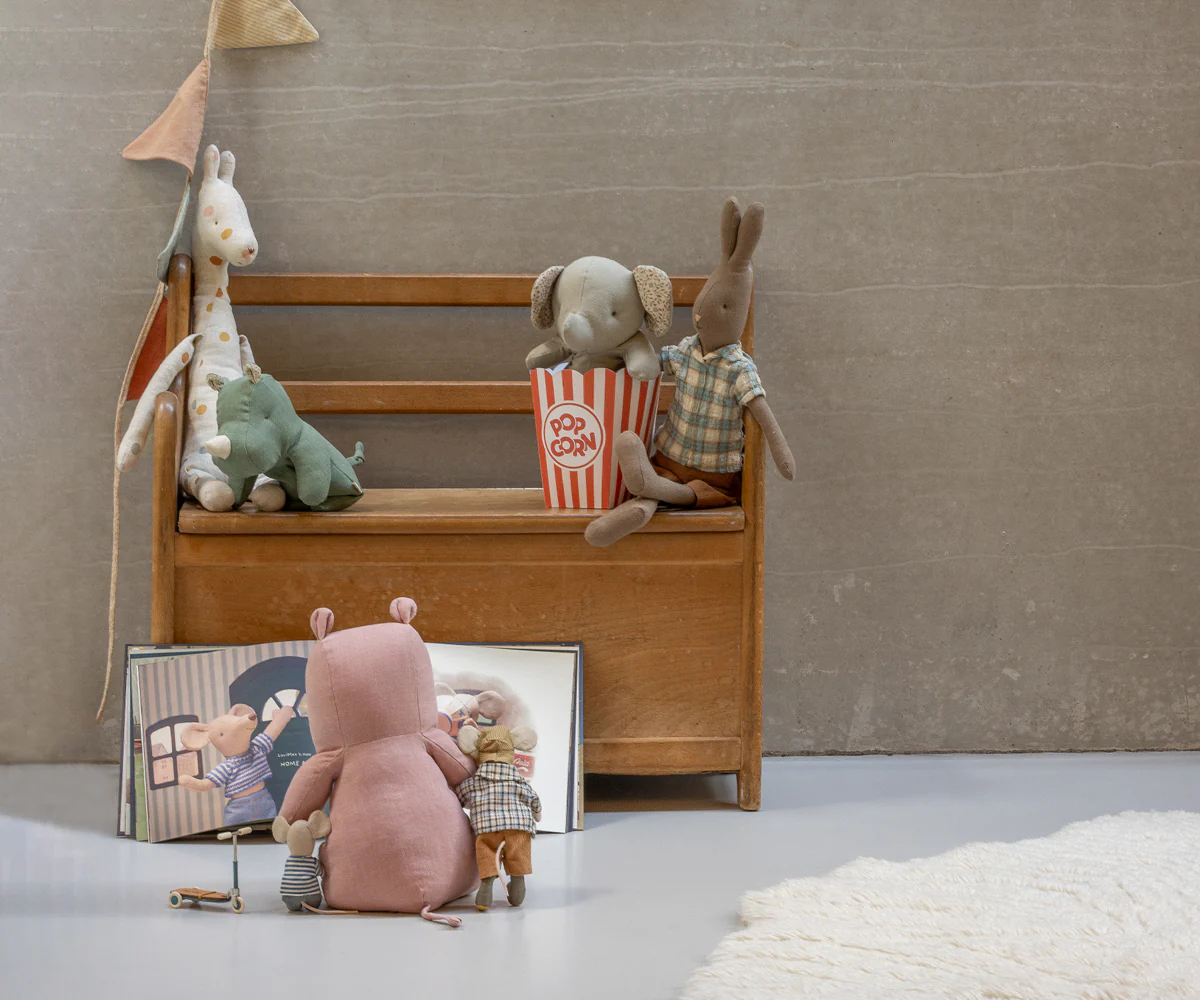 A stuffed animal toy sits on a wooden bench with popcorn and other toys in a cozy indoor setting.