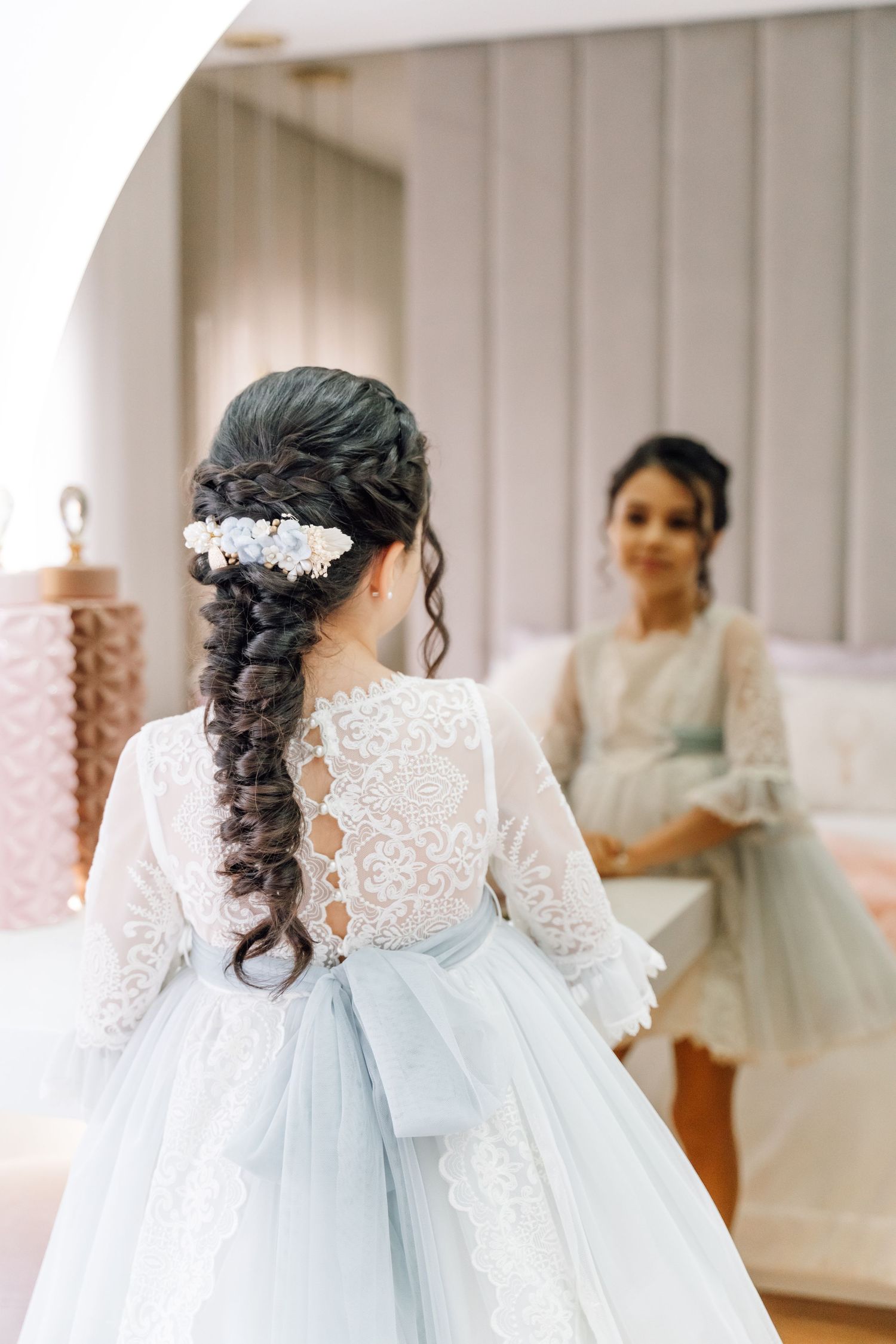 Elegant bridal hairstyle with long dark braids adorned with white flower accessories, shown from behind in a blue gown.