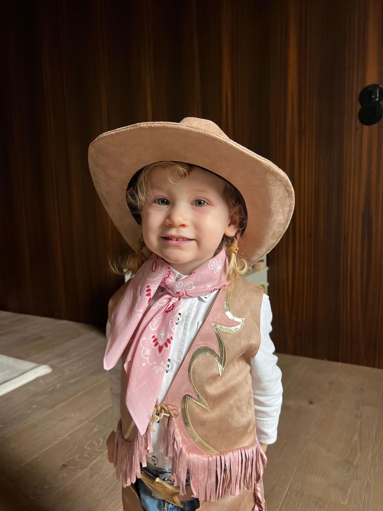 A child in a pink vest and cowboy hat poses playfully in multiple photos against a wooden wall background.