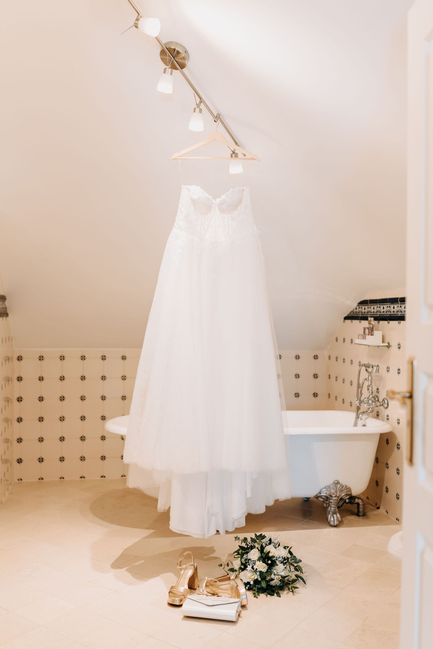 White wedding dress hangs elegantly from ceiling in minimalist bridal suite with cream walls and natural lighting.