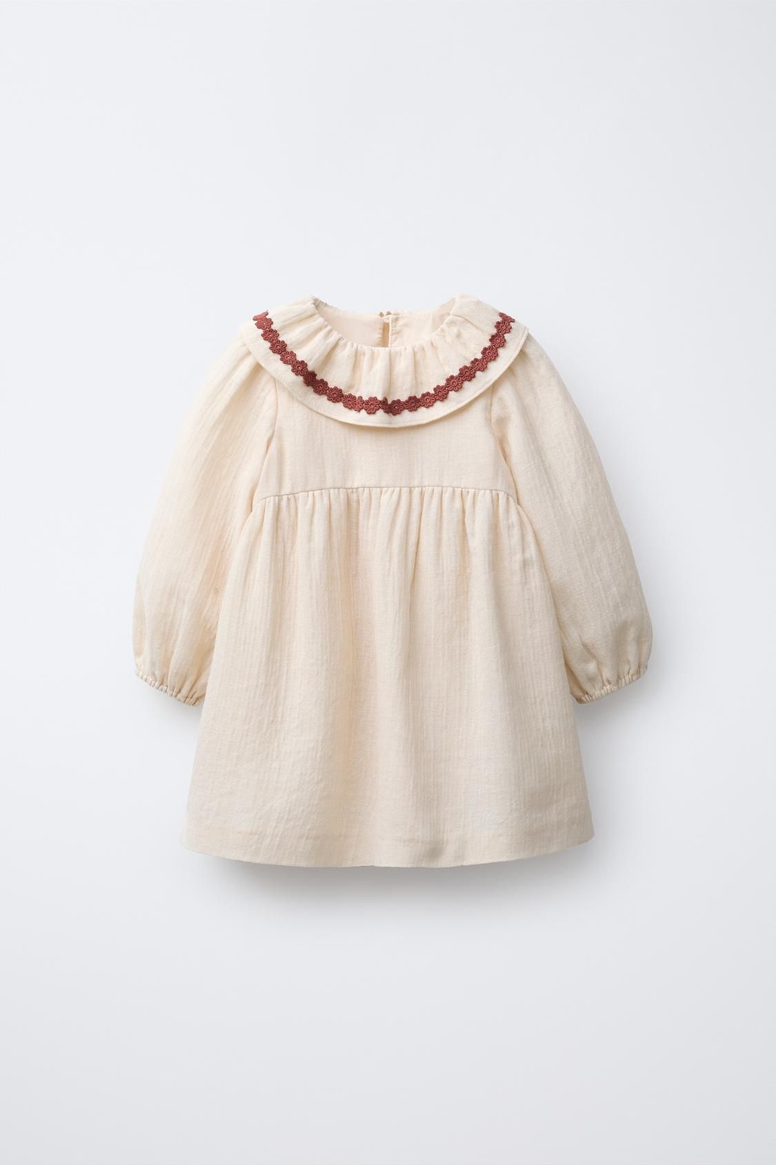 Sweet cream-colored baby blouse with puff sleeves and delicate burgundy trim along the neckline shows three views.