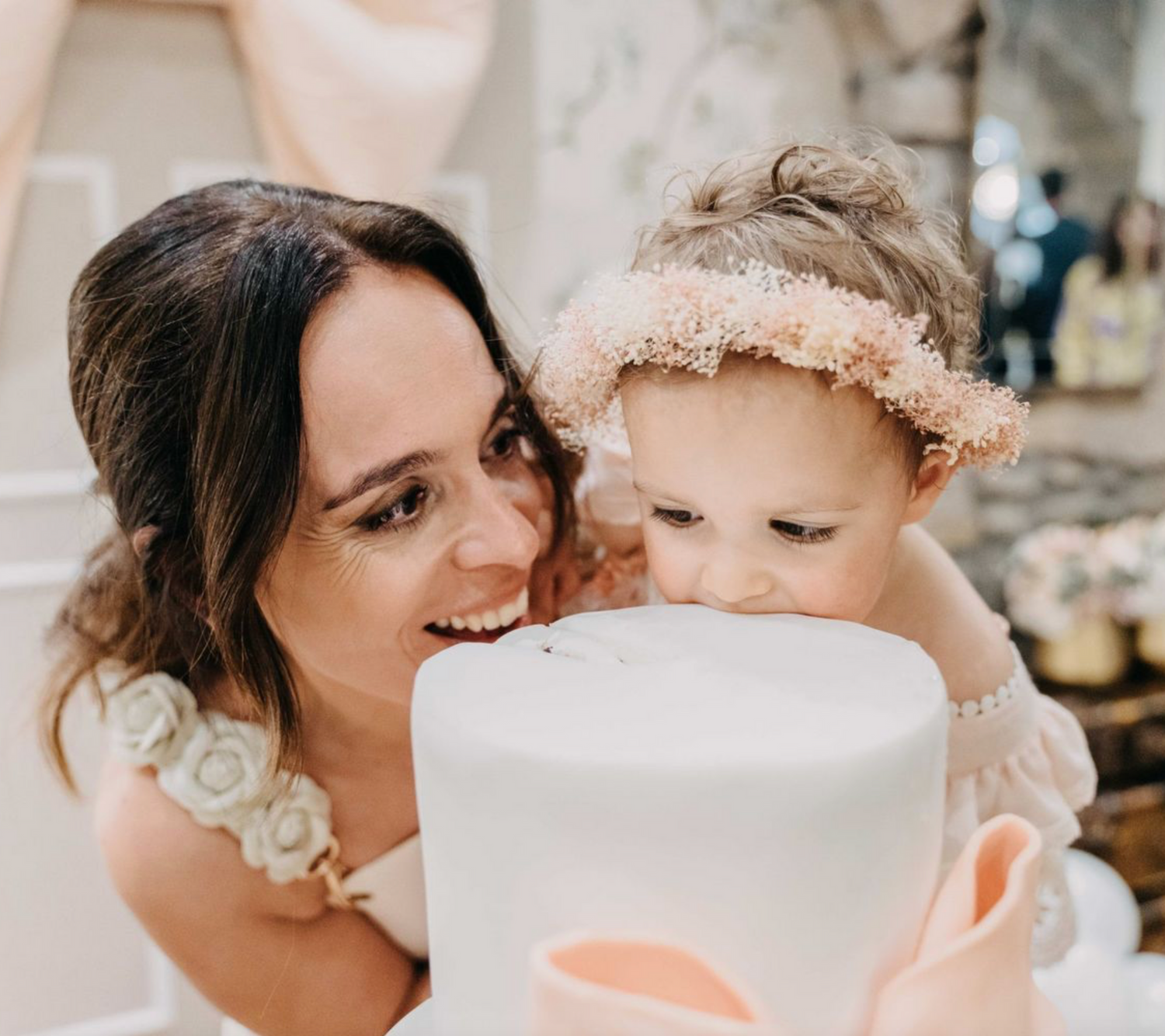 A gentle moment captured with a baby wearing a delicate lace headband leaning over a white cake.