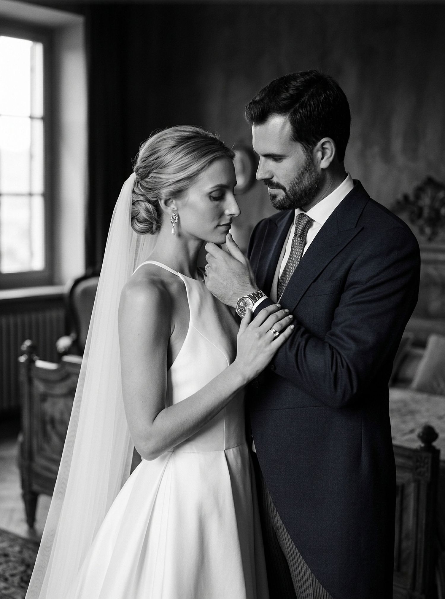 Black and white wedding portrait of bride in veil and groom in suit sharing an intimate moment indoors.