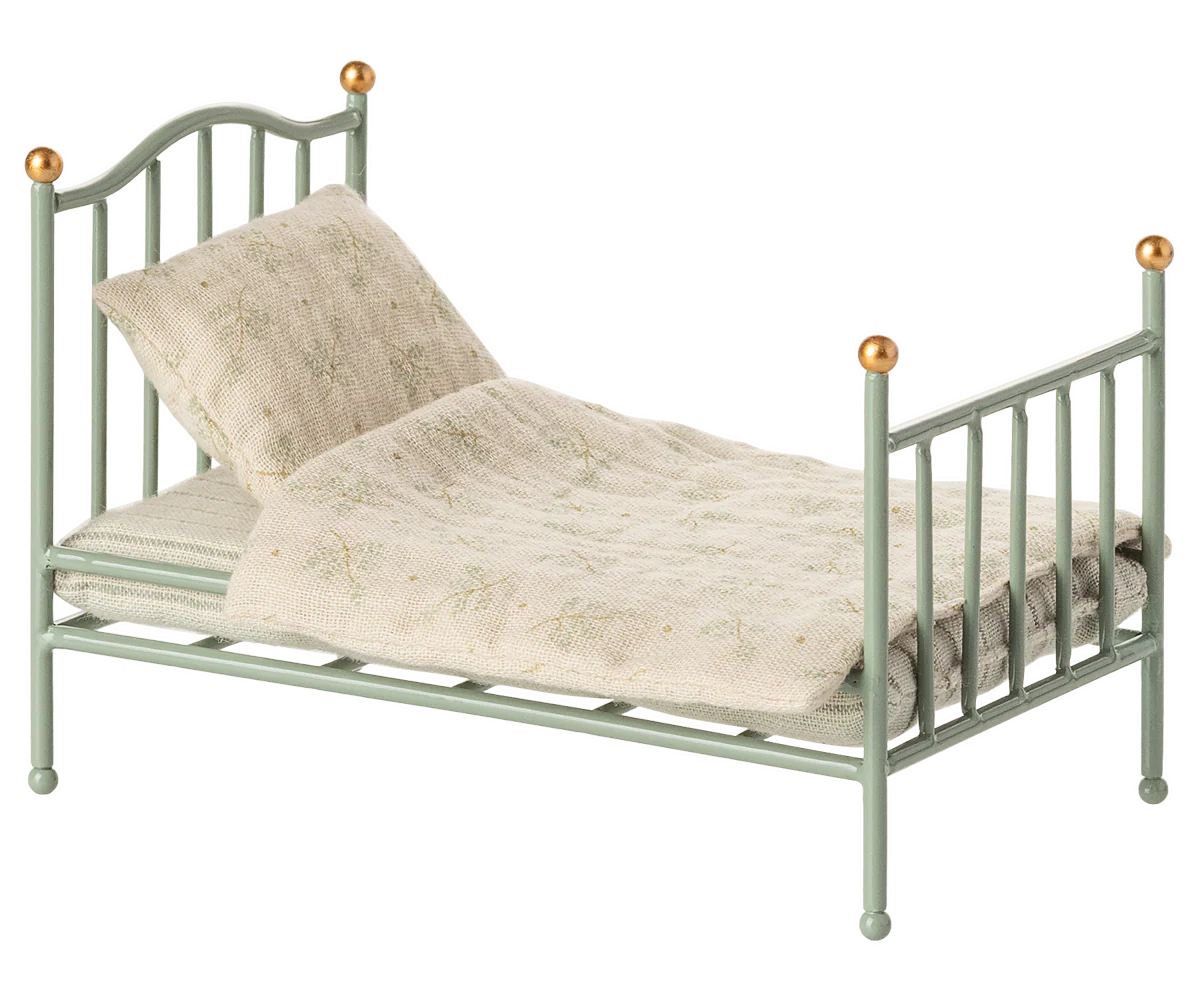 Vintage mint green metal doll bed with cream colored bedding and brass finial posts.