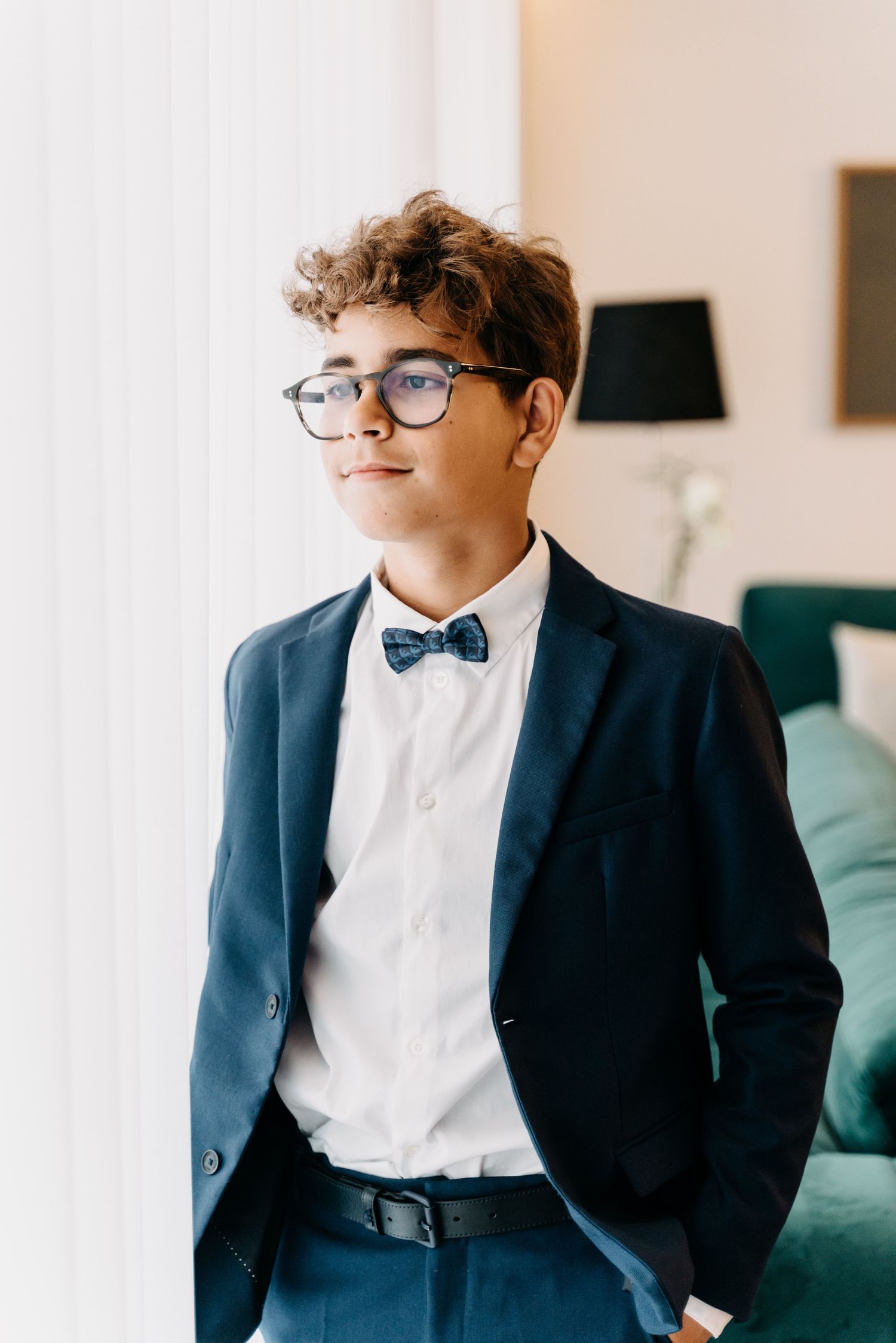 Stylish navy suit paired with polka dot bow tie, white dress shirt and glasses for formal attire.