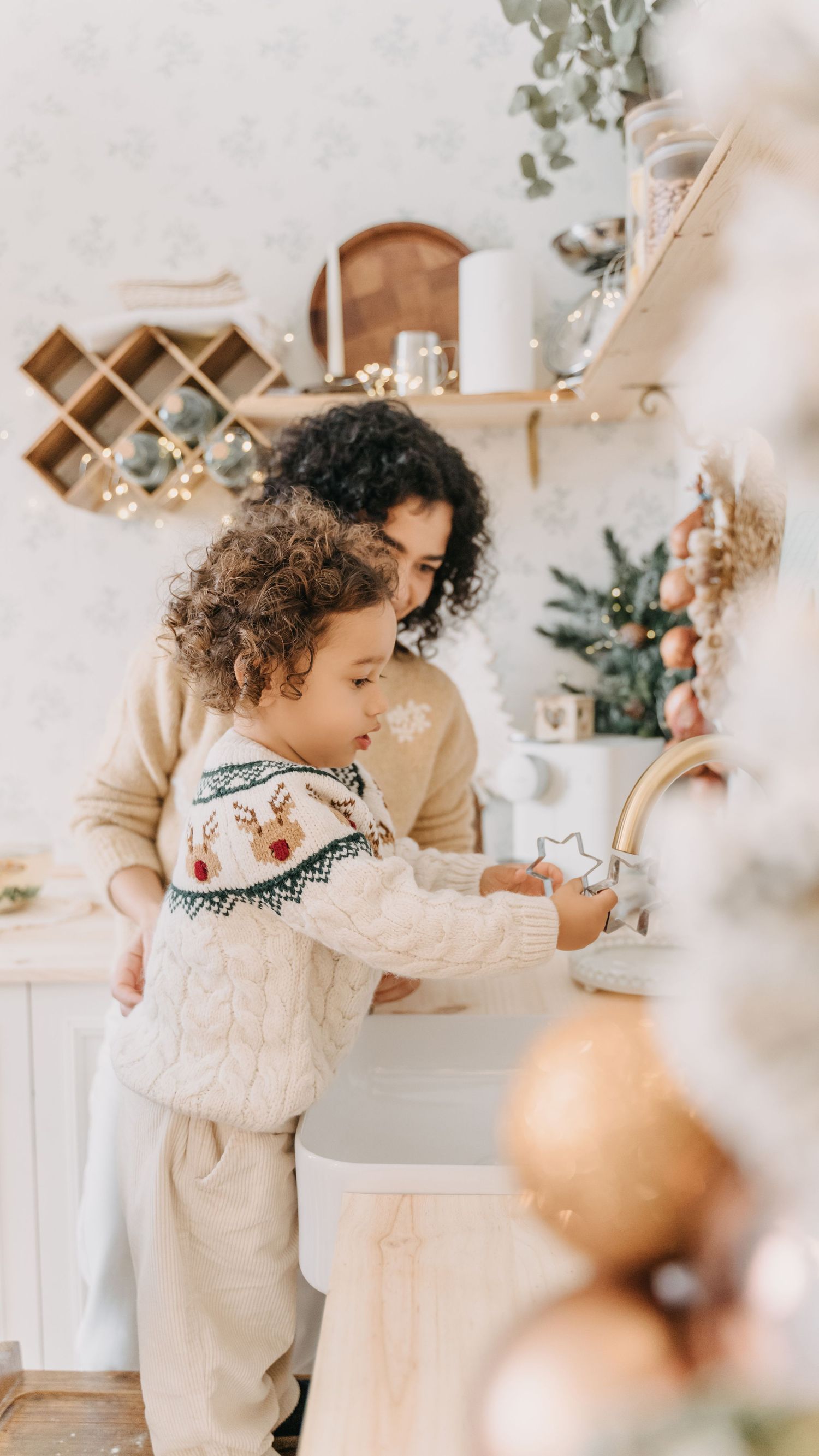 A toddler in neutral-colored clothing explores a minimalist room decorated with soft holiday accents and wooden details.