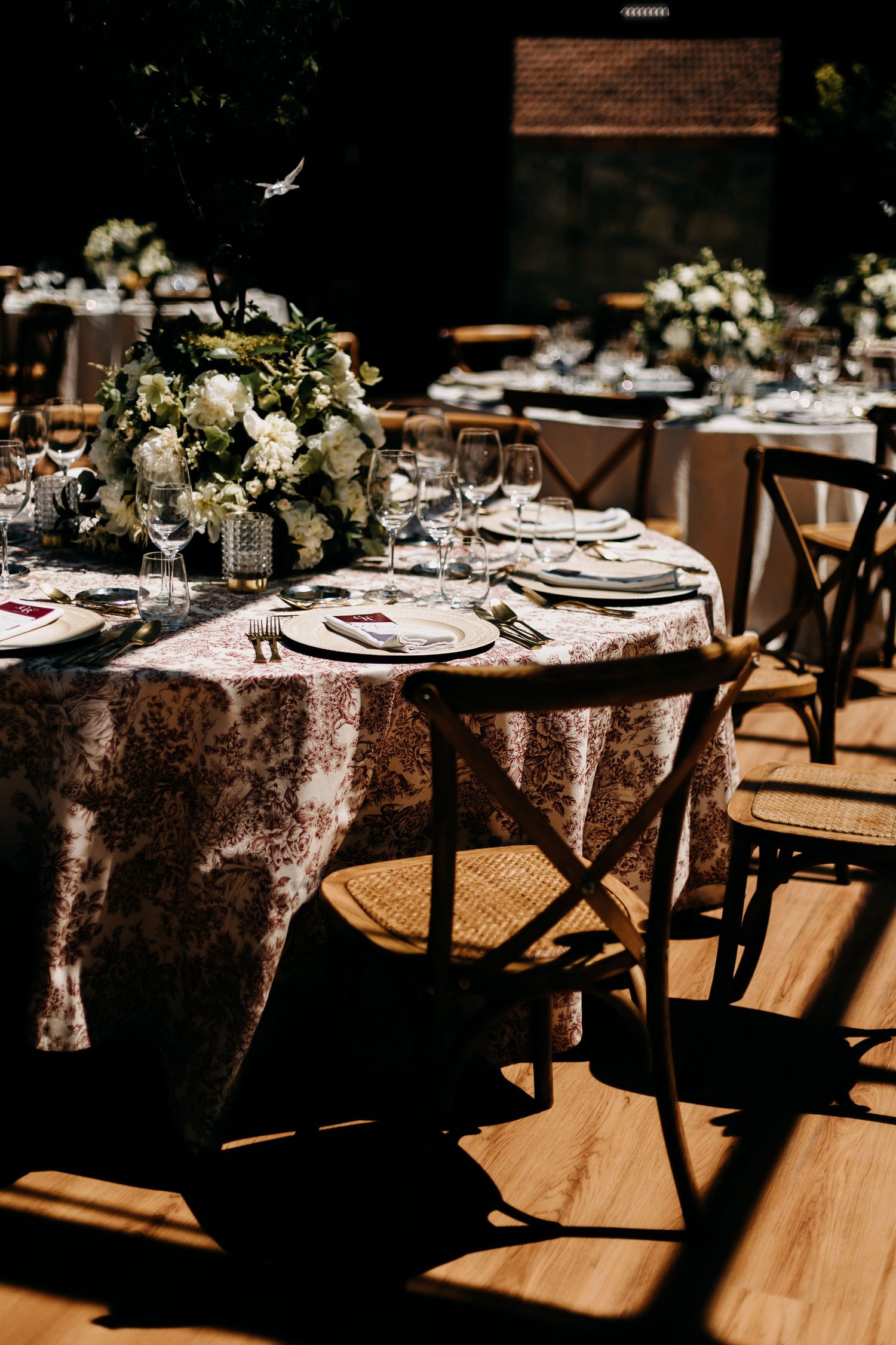 Elegant wedding reception tables with vintage brown linen tablecloths and place settings arranged in sunlit venue space.