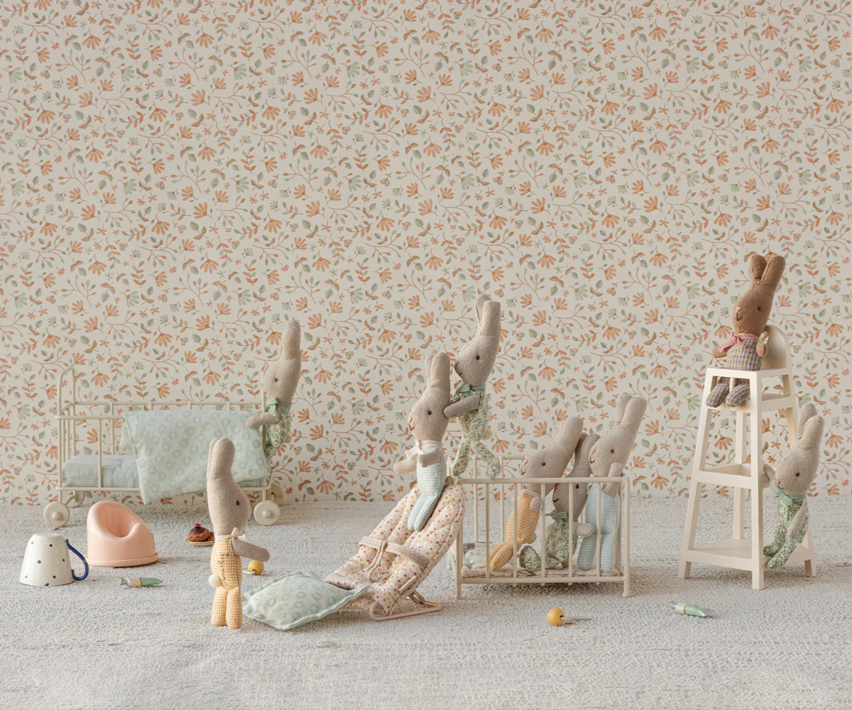 Soft pastel colored toys and miniature furniture arranged against a floral wallpaper background in a vintage nursery setting.