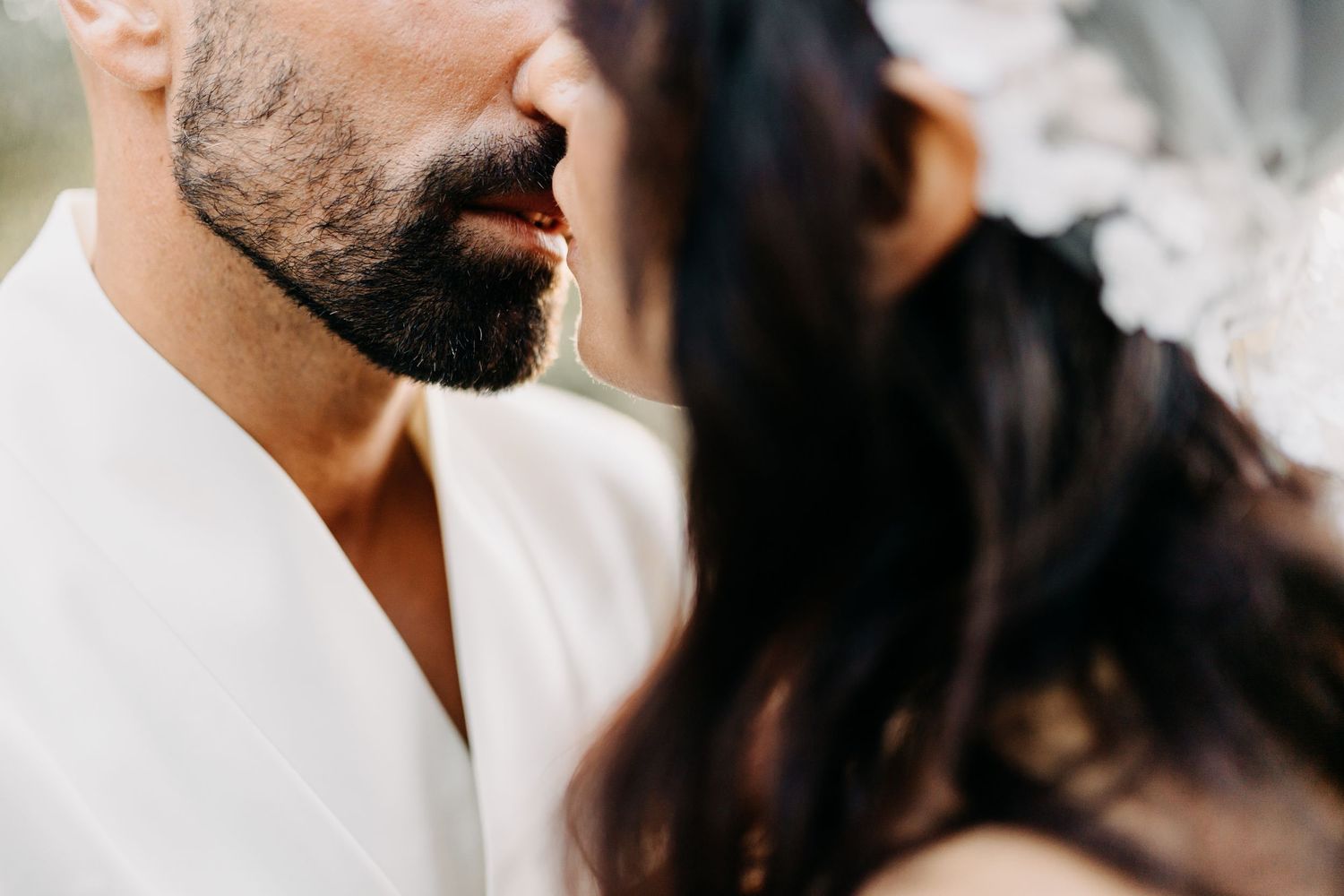 A couple in formal wedding attire shares a romantic moment outdoors in matching white outfits.