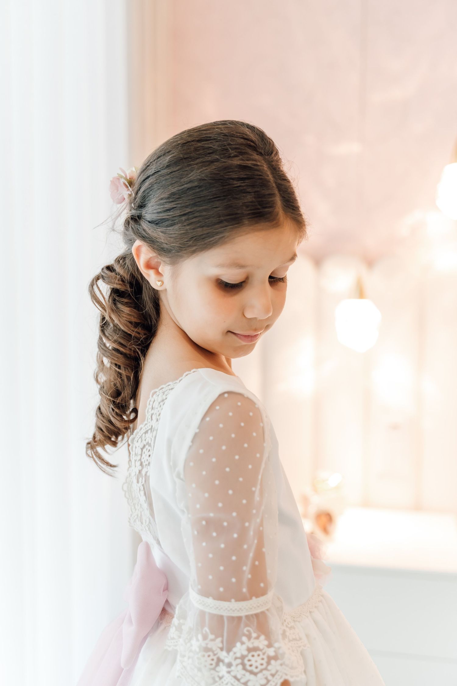 Young person in delicate white lace dress with sheer polka dot sleeves posed elegantly in soft natural light.