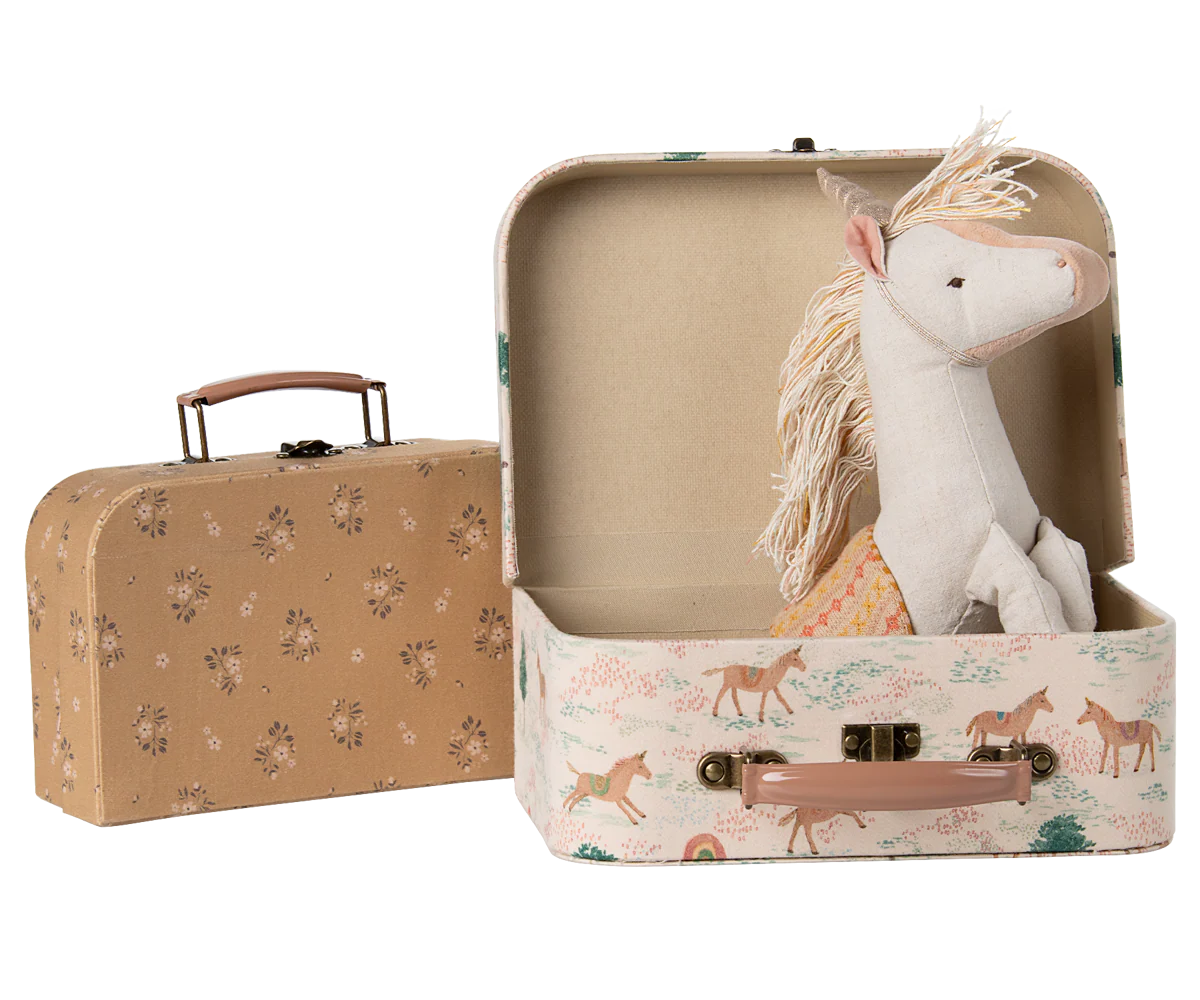 A series of beige leather suitcases and white stuffed animal toys arranged in a row on a white surface.