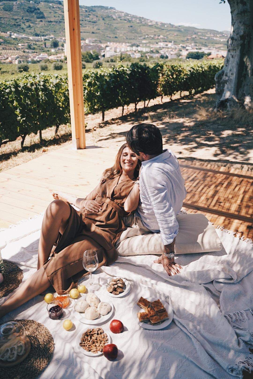 Couple enjoying romantic vineyard picnic with wine and snacks against mountain backdrop.